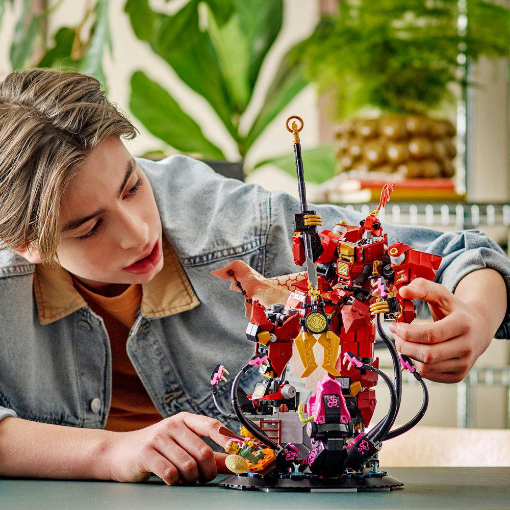 Ein Teenager baut einen roten LEGO-Roboter vor einem grünen Hintergrund.