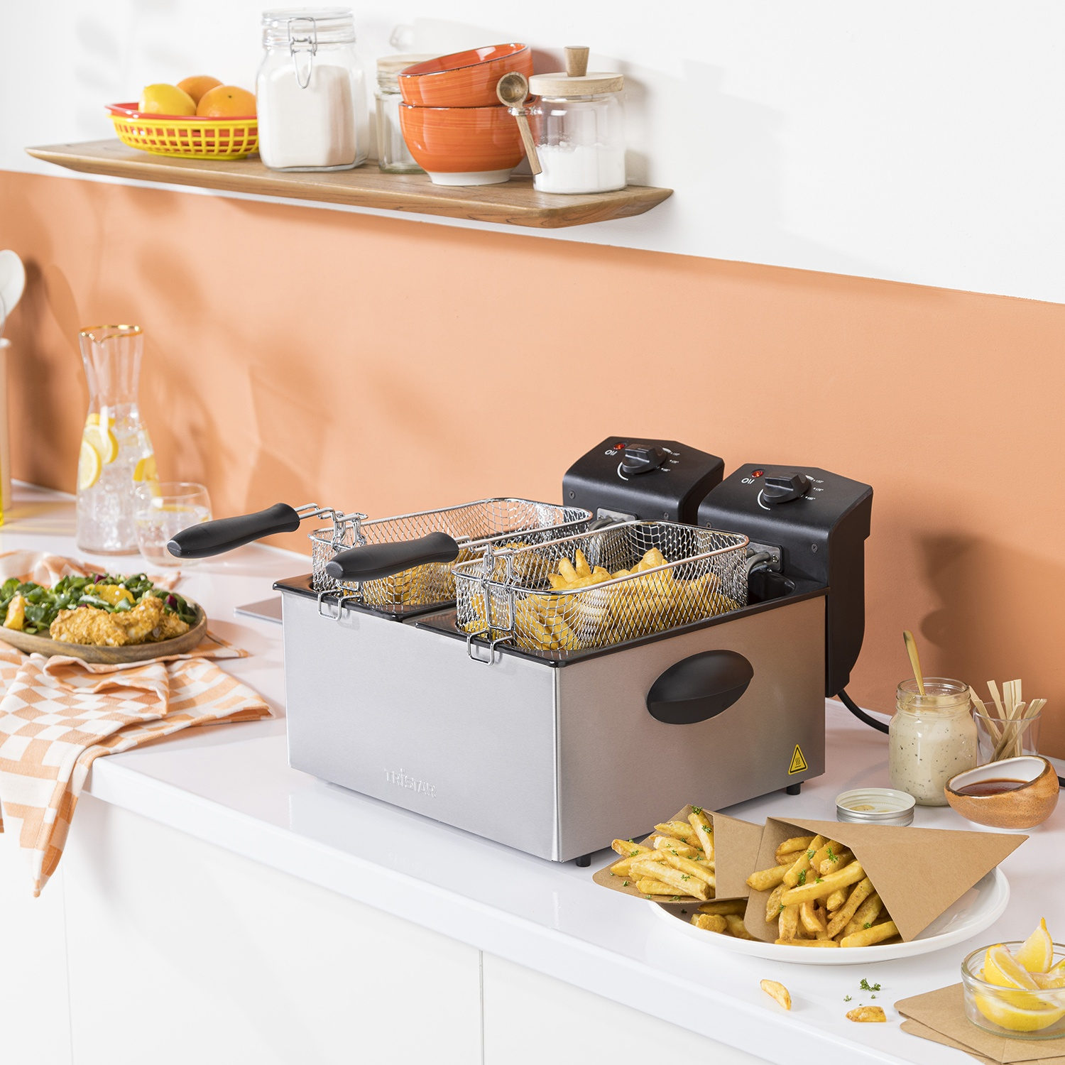 Una friggitrice con patatine fritte in una cucina, circondata da cibo e utensili.