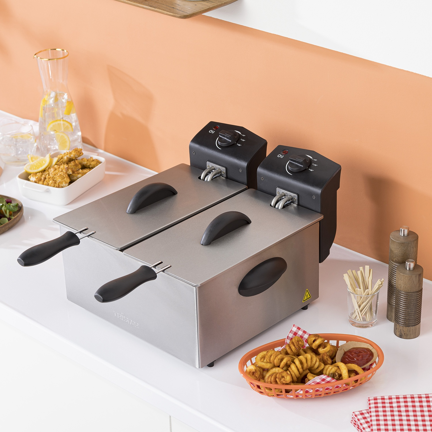 Friggitrice doppia in acciaio inox con cibo e bevande su un bancone bianco.