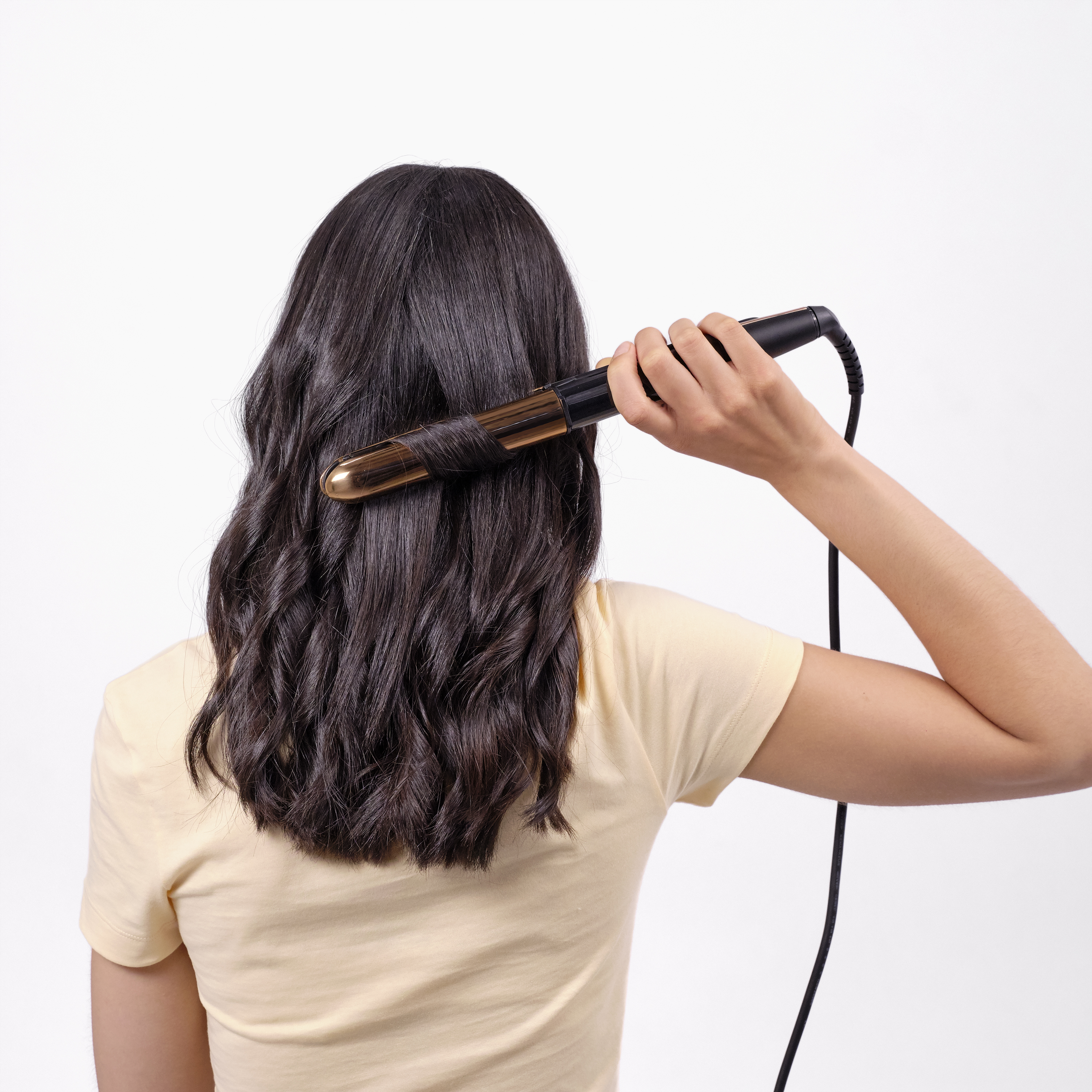 Una donna arriccia i suoi capelli scuri con un ferro arricciacapelli su uno sfondo bianco.