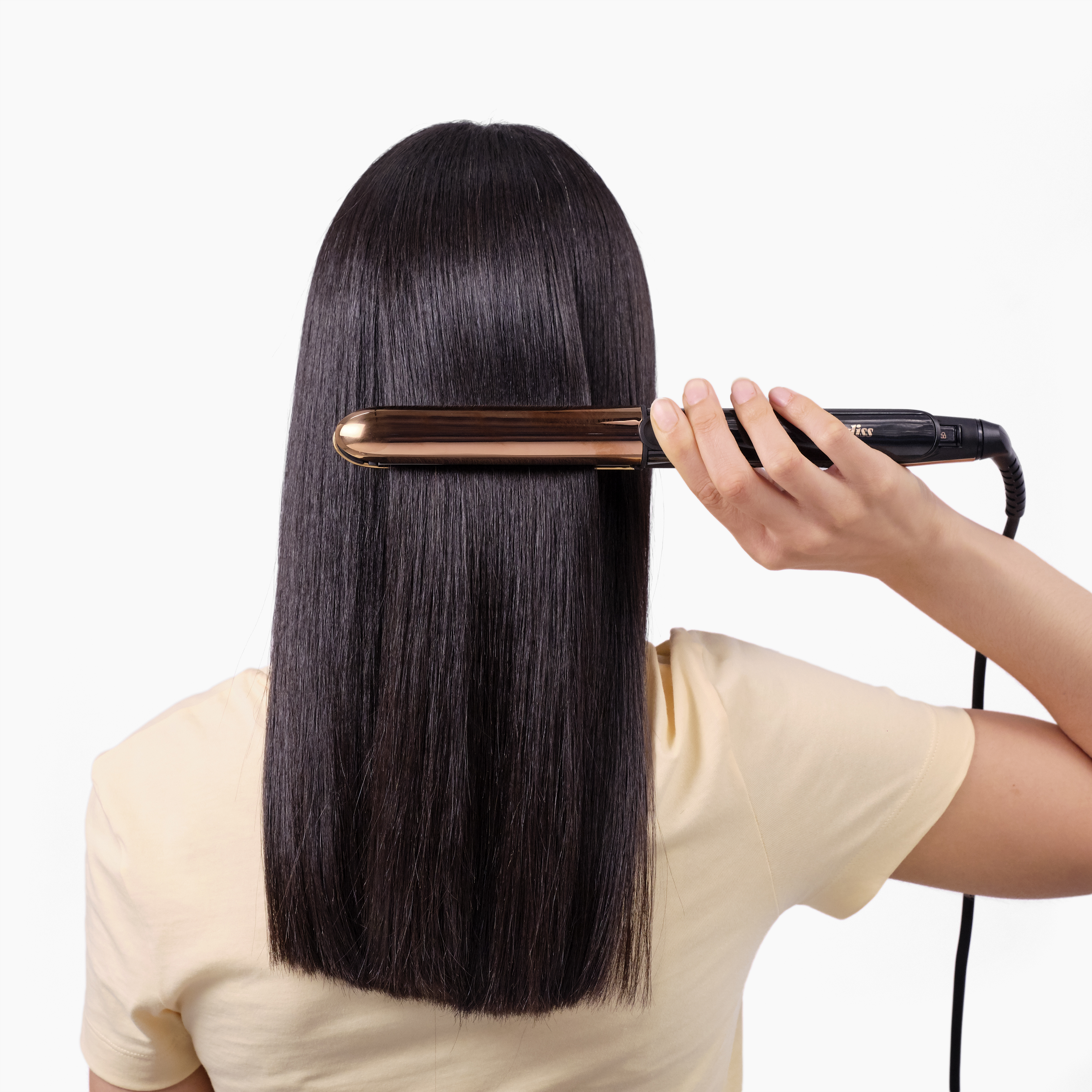 Una donna liscia i suoi capelli neri e lucenti con una piastra dorata su uno sfondo bianco.