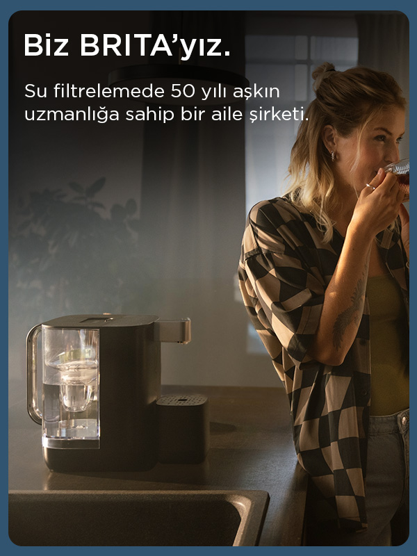 Bir kadın, siyah bir Brita su filtresinin yanında içiyor. Cihaz, koyu renkli bir tezgahın üzerinde duruyor.