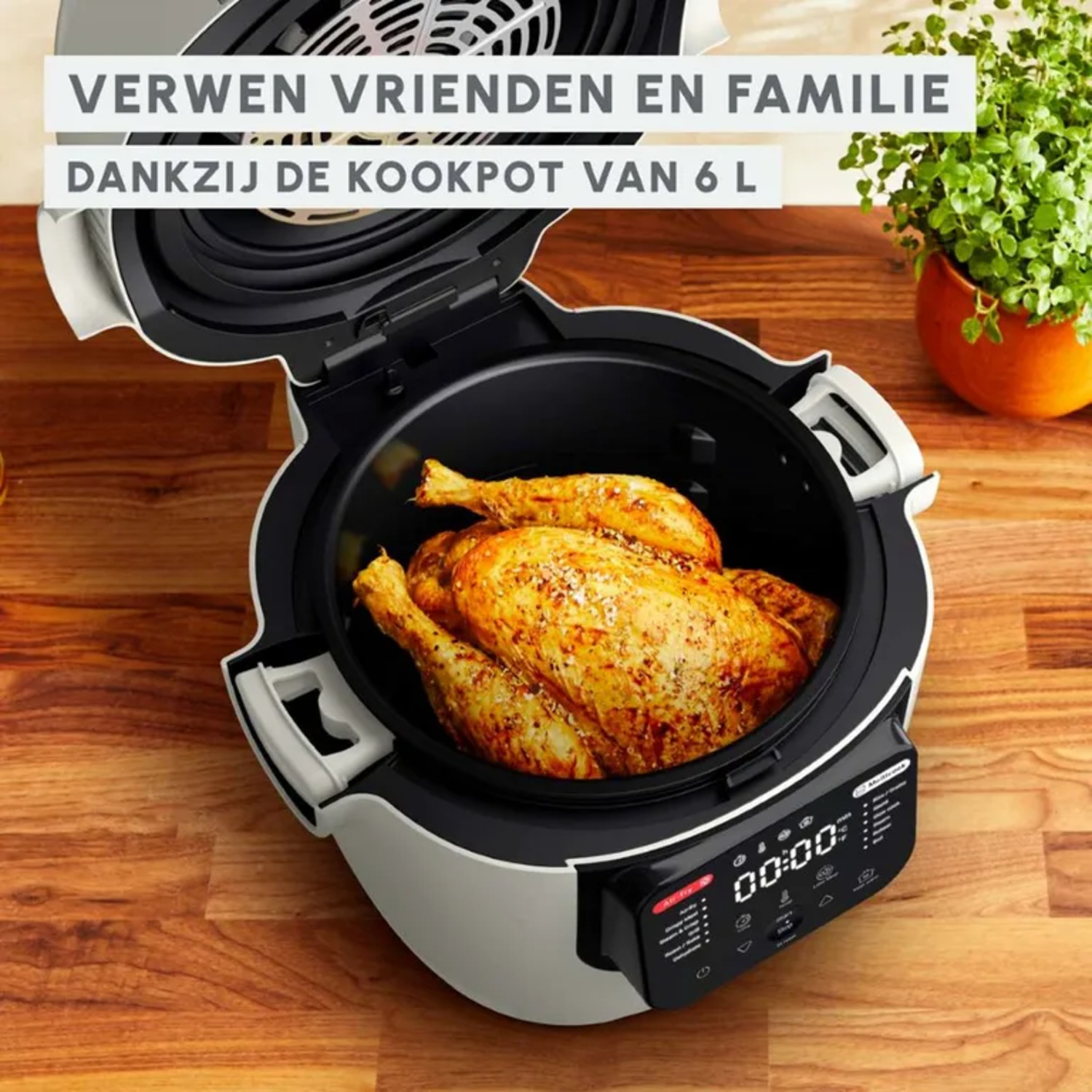 An air fryer with a roasted chicken inside, on a wooden table, next to a plant.