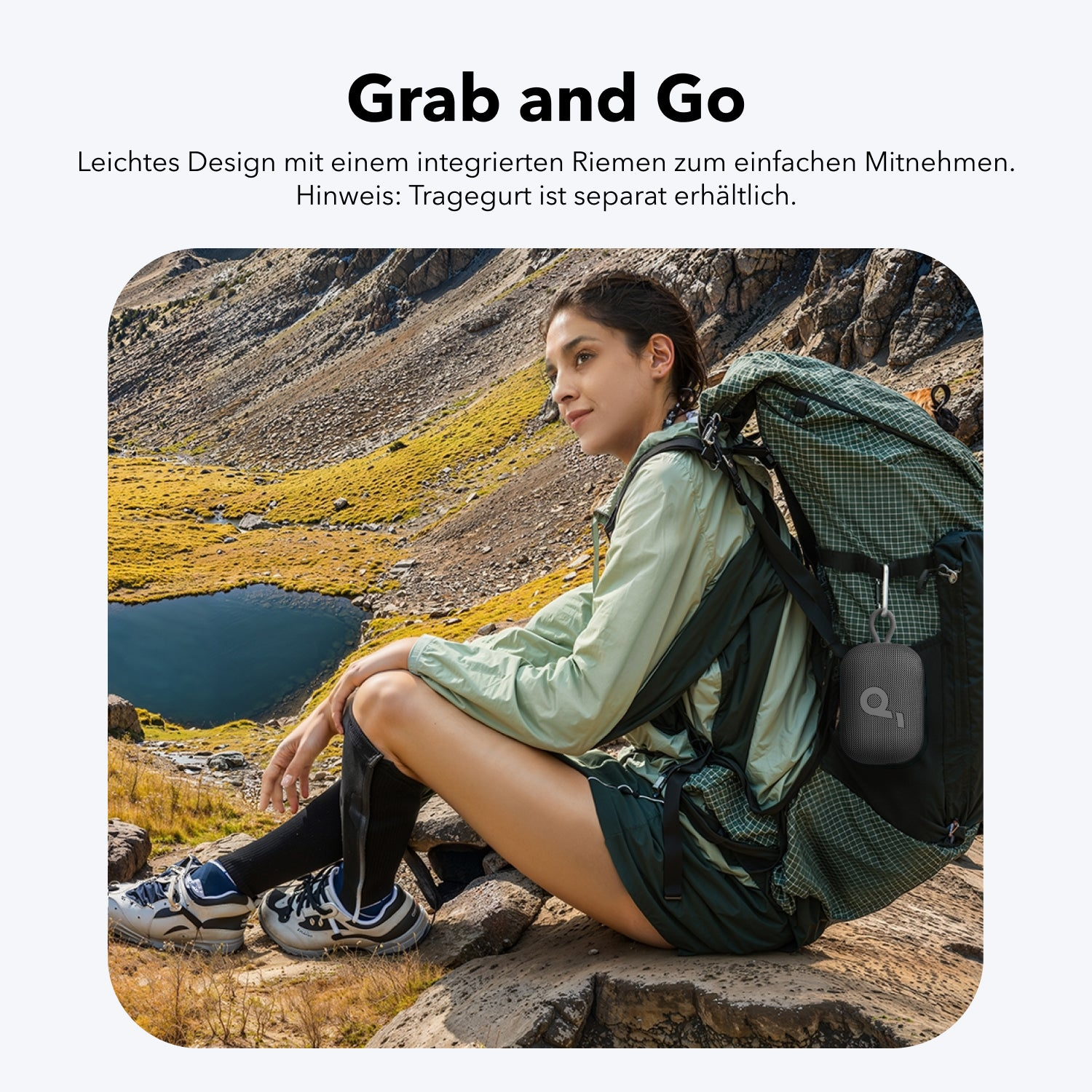 Frau mit Rucksack sitzt vor Bergsee, trägt grüne Jacke und dunkle Shorts.