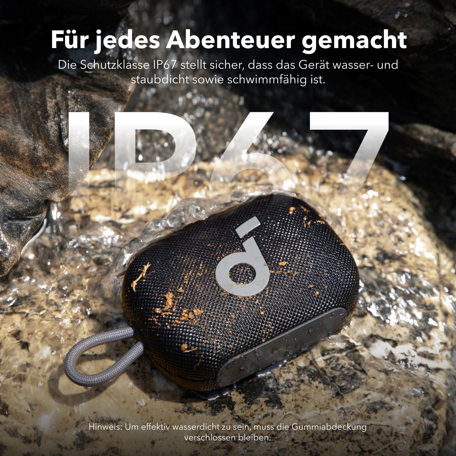 Schwarzer Lautsprecher mit grauem Band liegt auf einem Stein im Wasser, staubbedeckt.