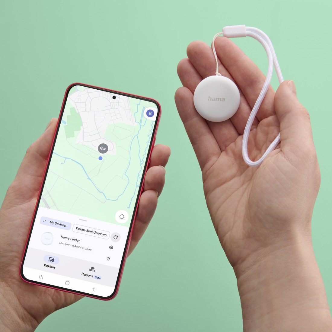 Eine Person hält ein Smartphone mit einer Karten-App und einen Hama-Tracker vor einem grünen Hintergrund.