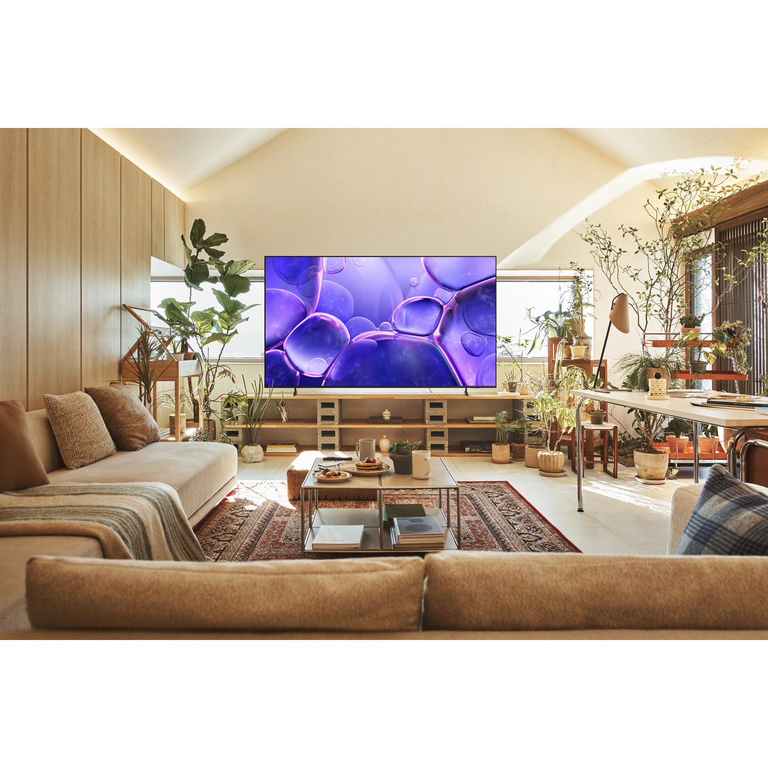 Living room with a beige couch, plants, and a TV displaying purple bubbles on the screen.