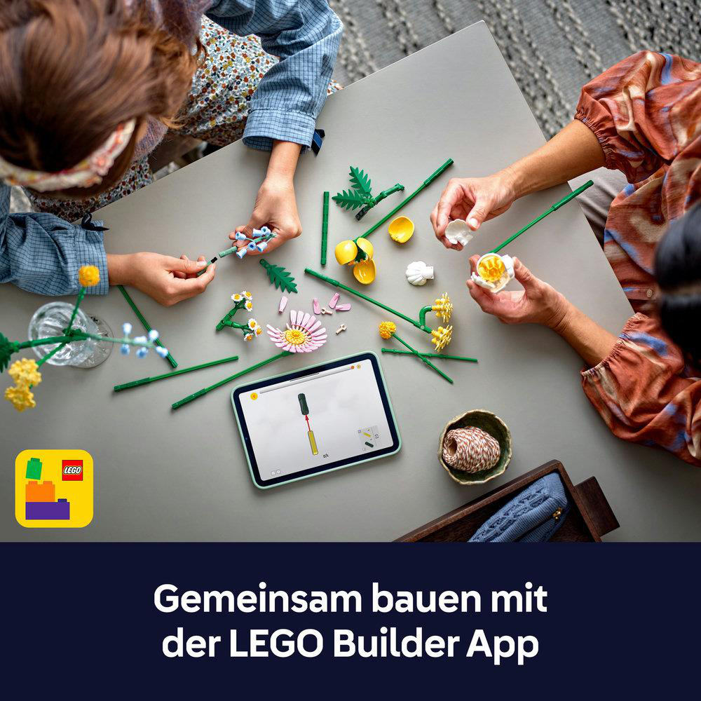 Personen bauen LEGO Blumen mit einer App auf einem Tablet. Bunte Teile liegen auf dem Tisch.