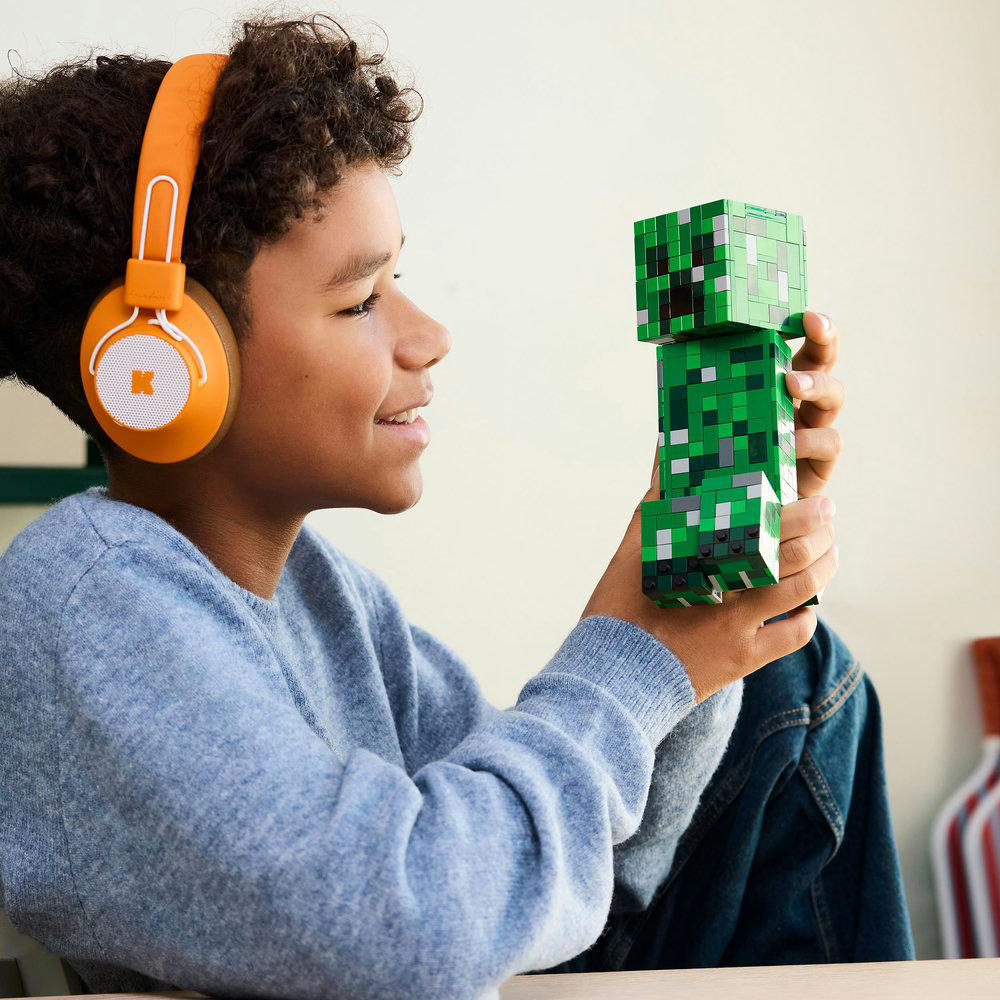Ein Junge mit orangefarbenen Kopfhörern betrachtet eine grüne Minecraft-Creeper-Figur.