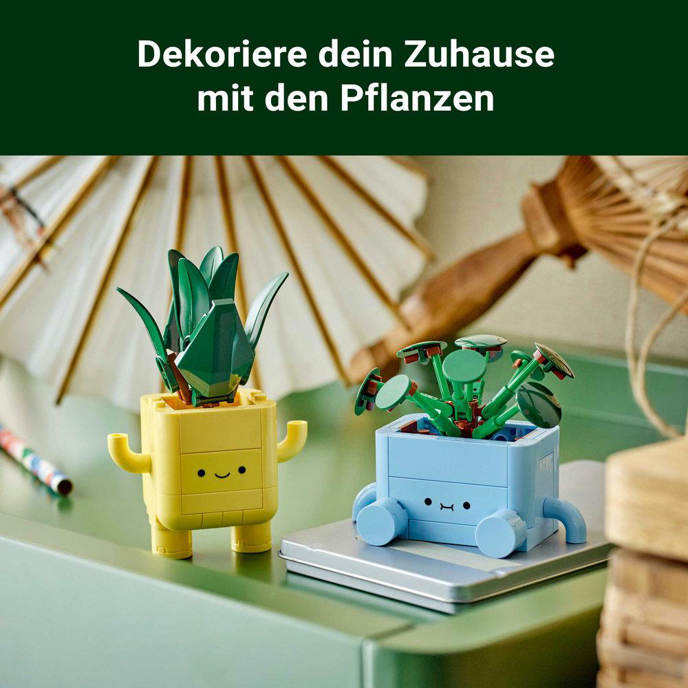 Zwei LEGO-Pflanzenfiguren in gelben und blauen Töpfen auf einem grünen Tisch vor einem weißen Schirm.
