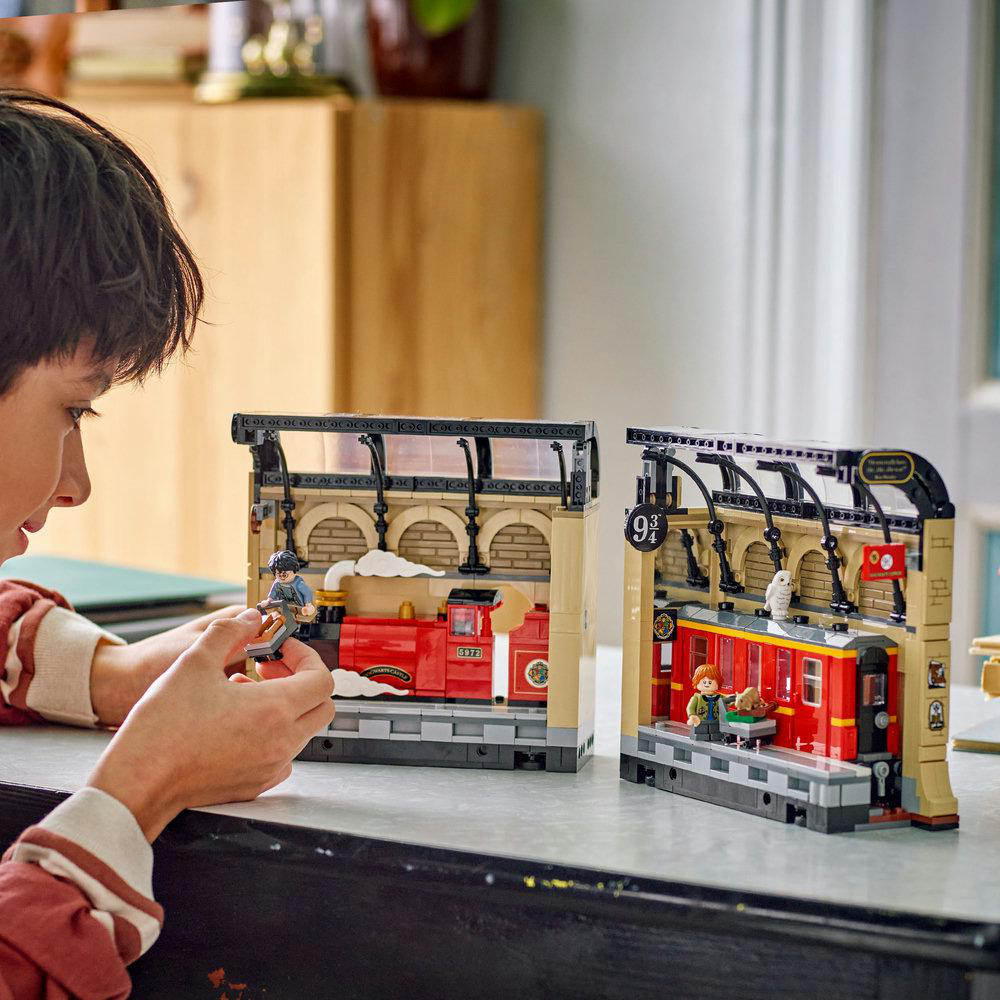 Ein Junge spielt mit Lego-Sets von Hogwarts Express auf Bahnsteig 9 3/4, mit roten Zügen und Figuren.