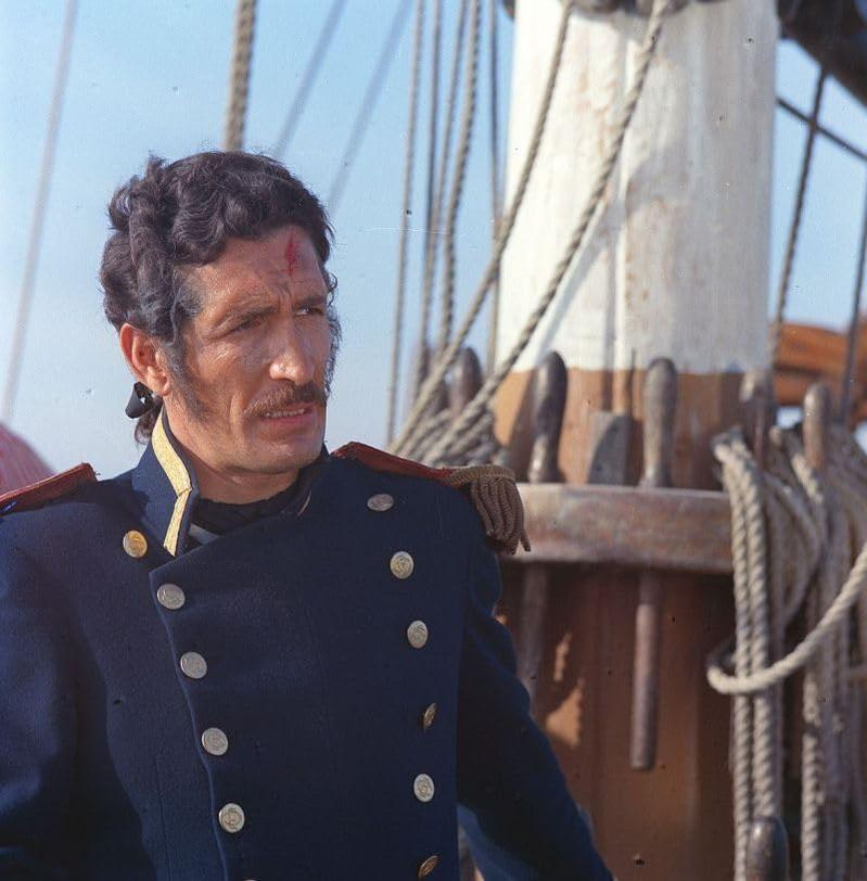 Ein Mann in Marineuniform, mit einem blutigen Kratzer im Gesicht, auf einem Schiff.