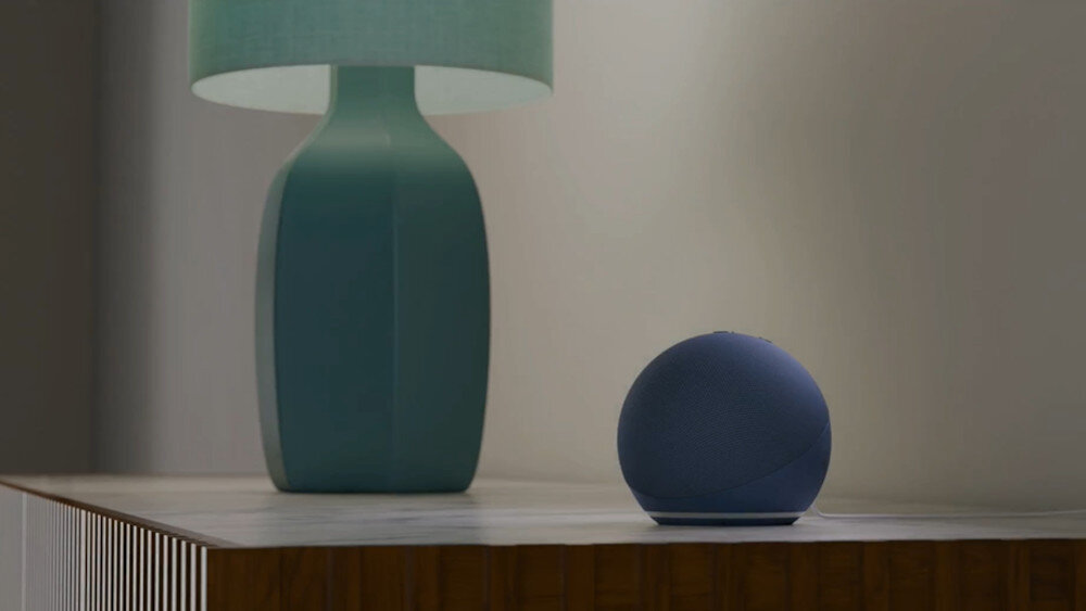 Niebieski głośnik na drewnianej powierzchni, z zieloną lampą w tle.