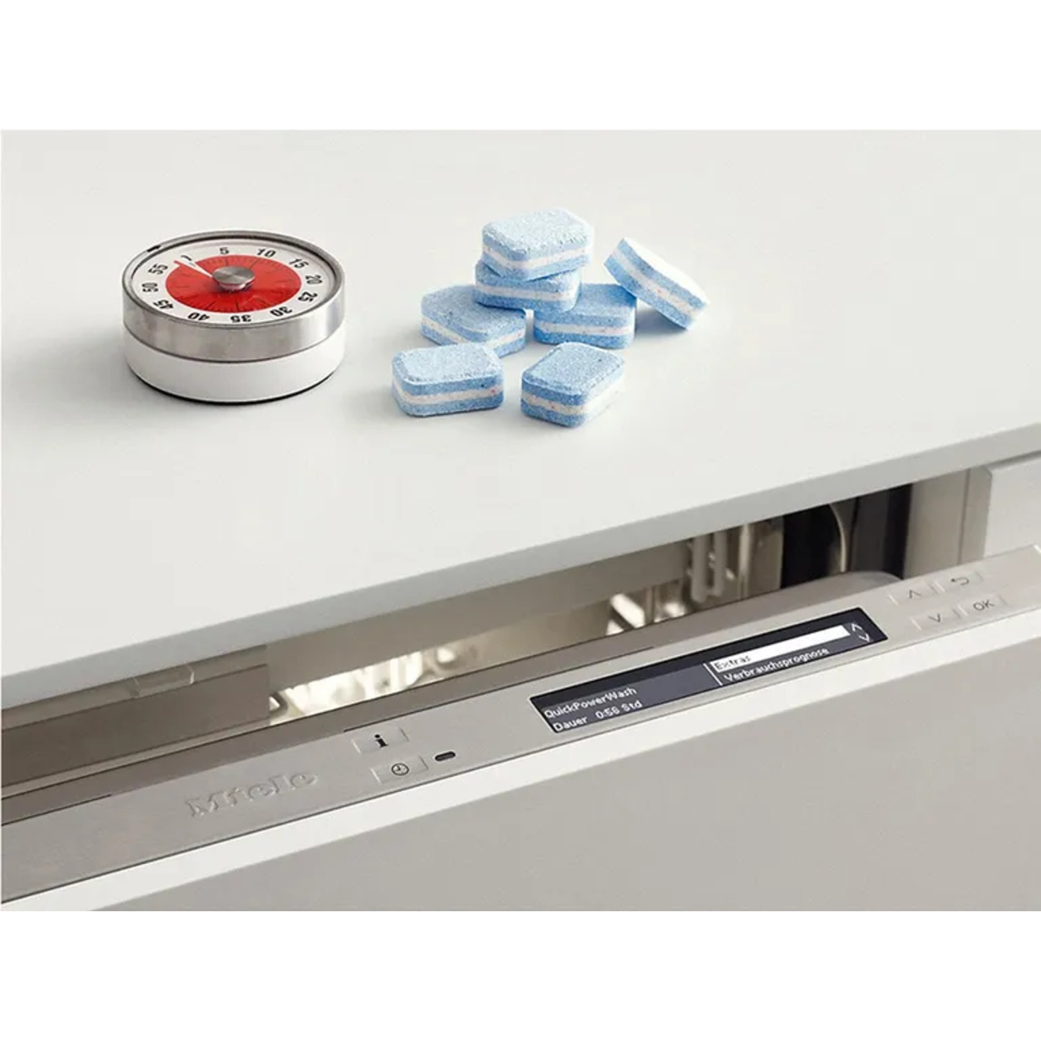 Dishwasher and timer. Blue and white tablets are on the counter. The dishwasher is open.