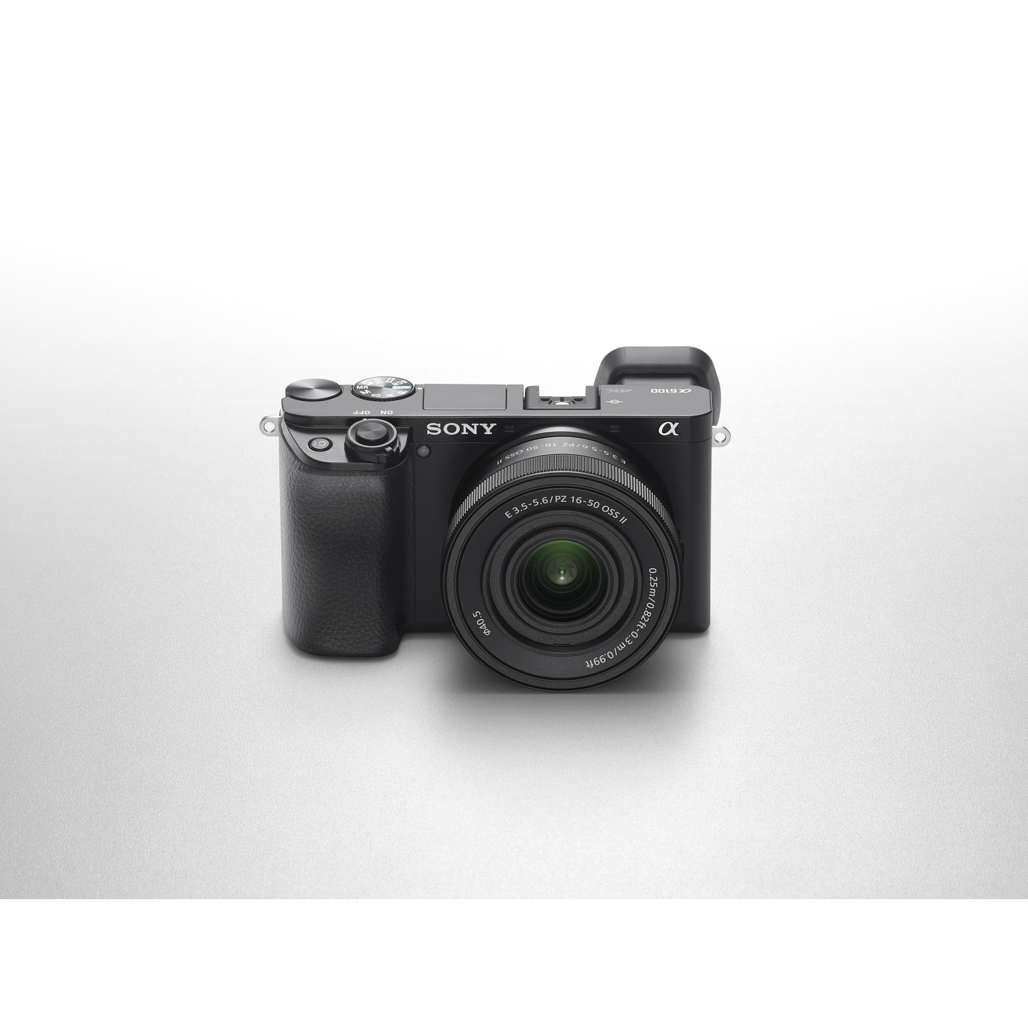 A black Sony α6100 camera is centered on a light gray surface. The lens is prominent, with details of the lens and camera body visible.