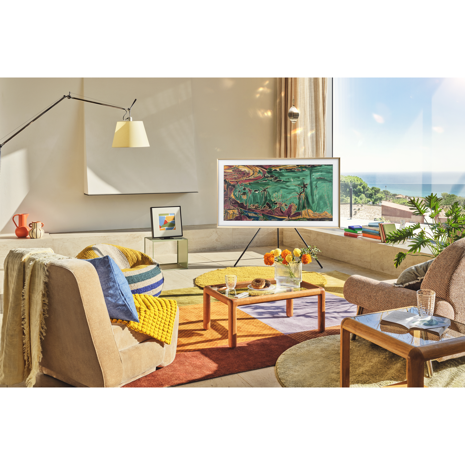 A modern living room with a TV displaying art, surrounded by furniture, a rug, and a window overlooking the sea.