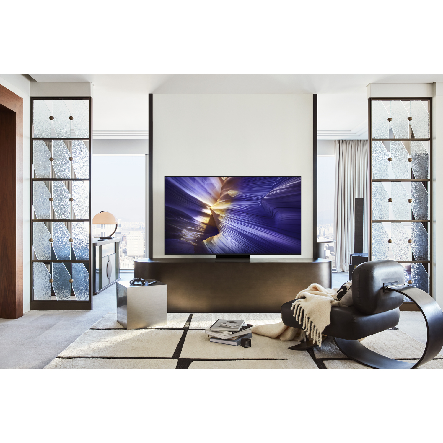 Salon avec une grande télévision sur un support marron foncé, des étagères en verre et un tapis.