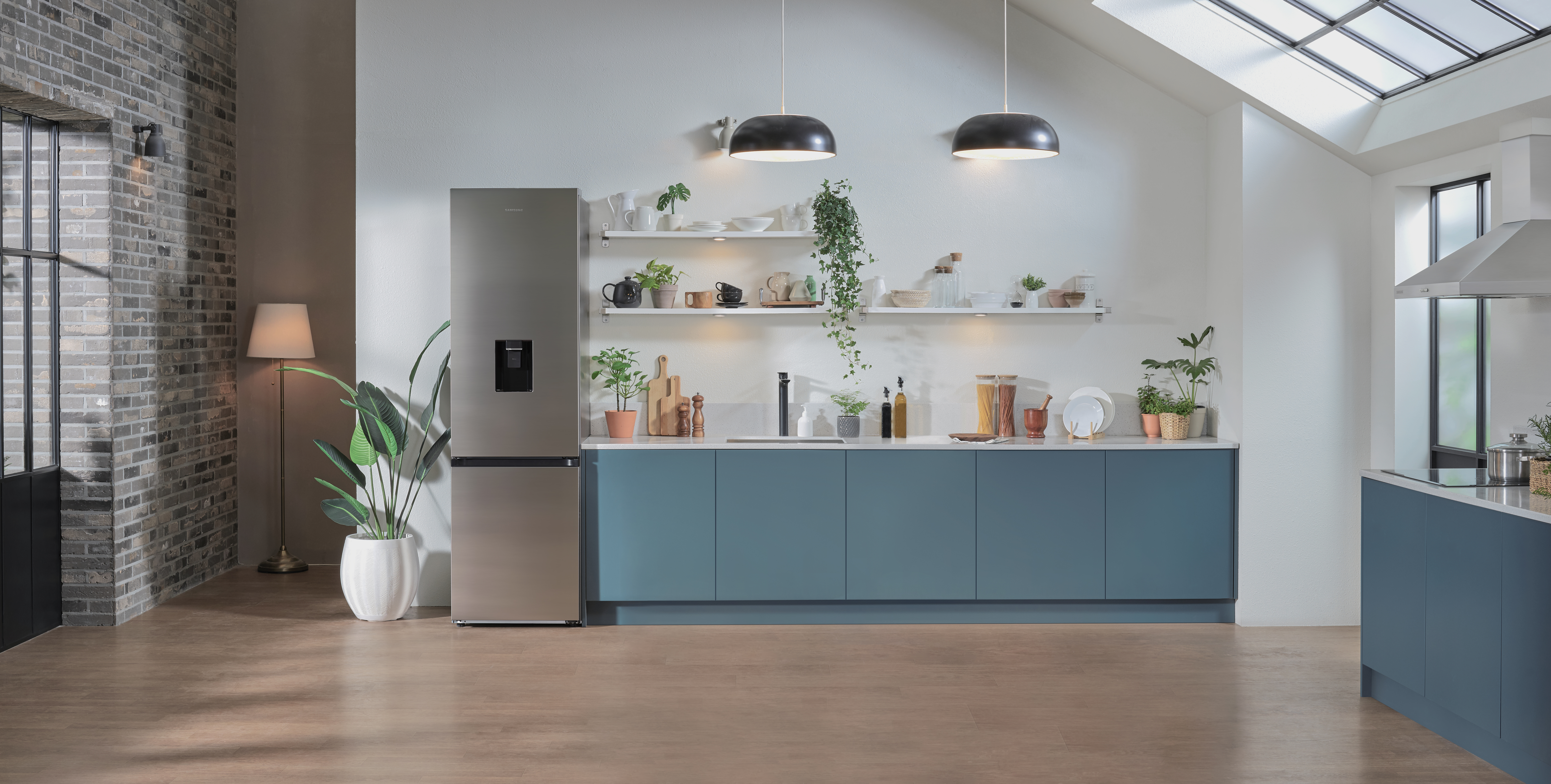 Kitchen with a refrigerator, cabinets, and plants. Two pendant lamps and a door are also visible.