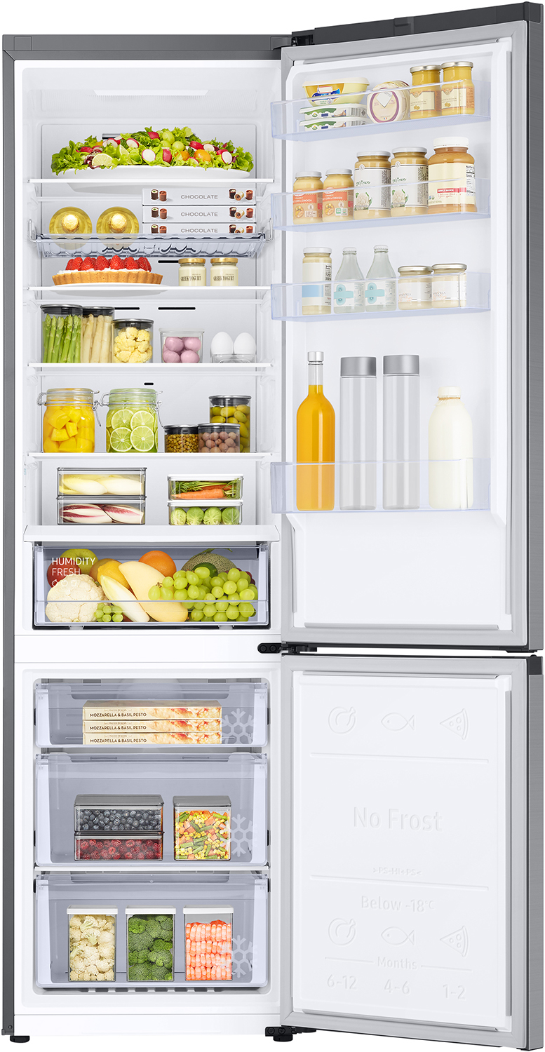 Refrigerator open, filled with food. Vegetables, fruits, drinks, and other groceries are visible on shelves and drawers.