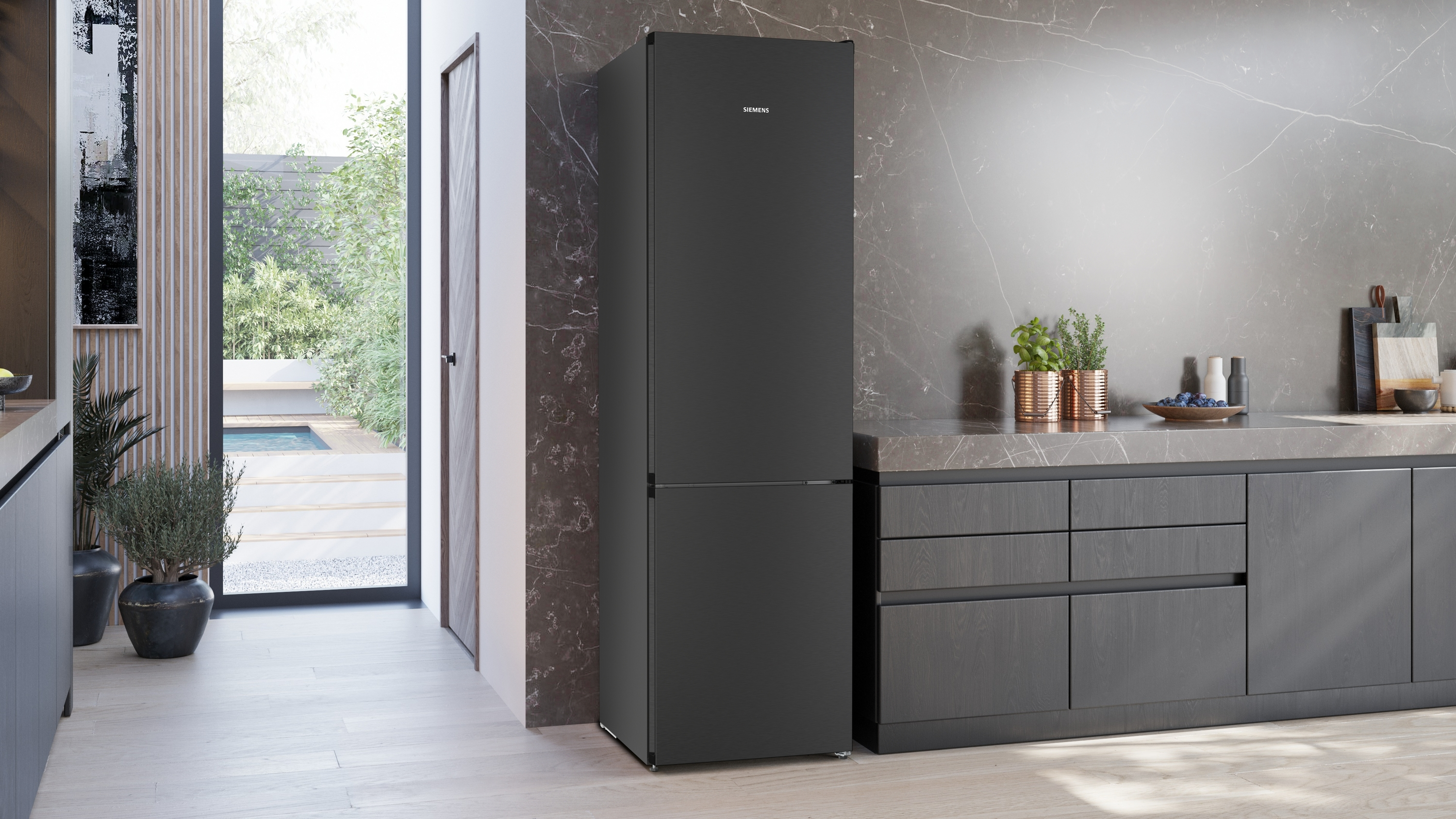 Eine schwarze Siemens-Kühlschrank steht in einer modernen Küche. Im Hintergrund ist ein Garten durch ein Fenster zu sehen.