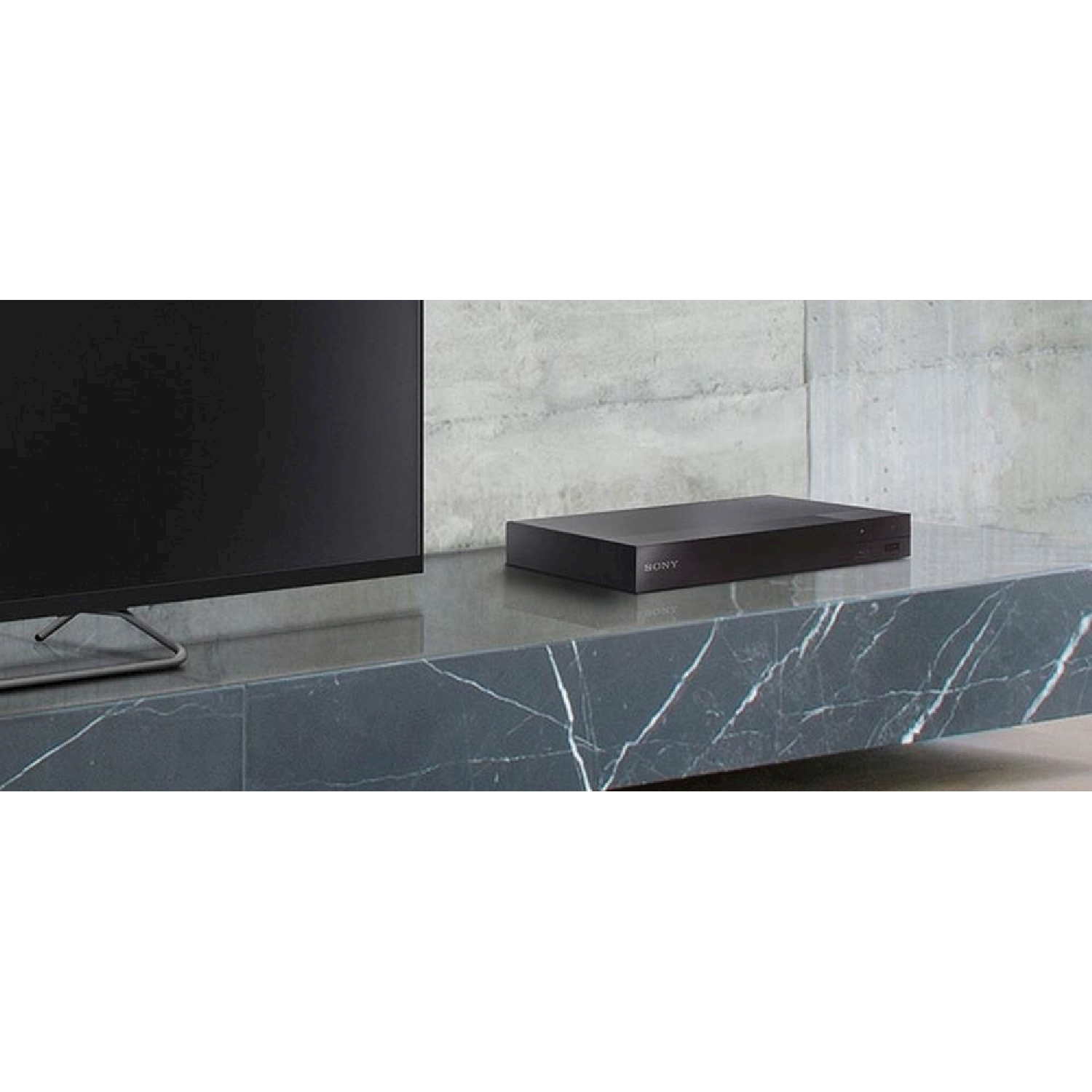 Un lettore Blu-ray nero è posizionato su un tavolo di fronte a un televisore, con il logo Sony.