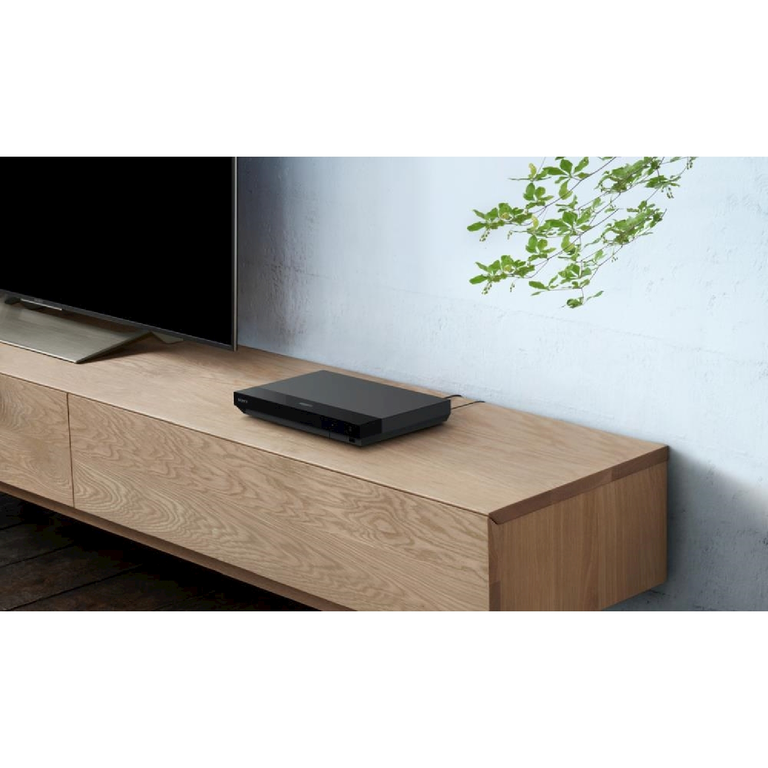 Lettore Blu-ray nero su un mobile in legno. TV e muro sullo sfondo.