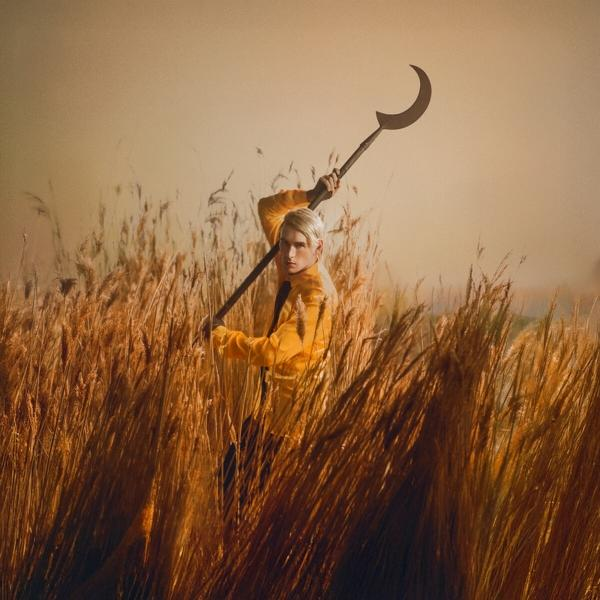 Eine Person in einem gelben Anzug, die ein sichelförmiges Werkzeug in einem Feld hält.