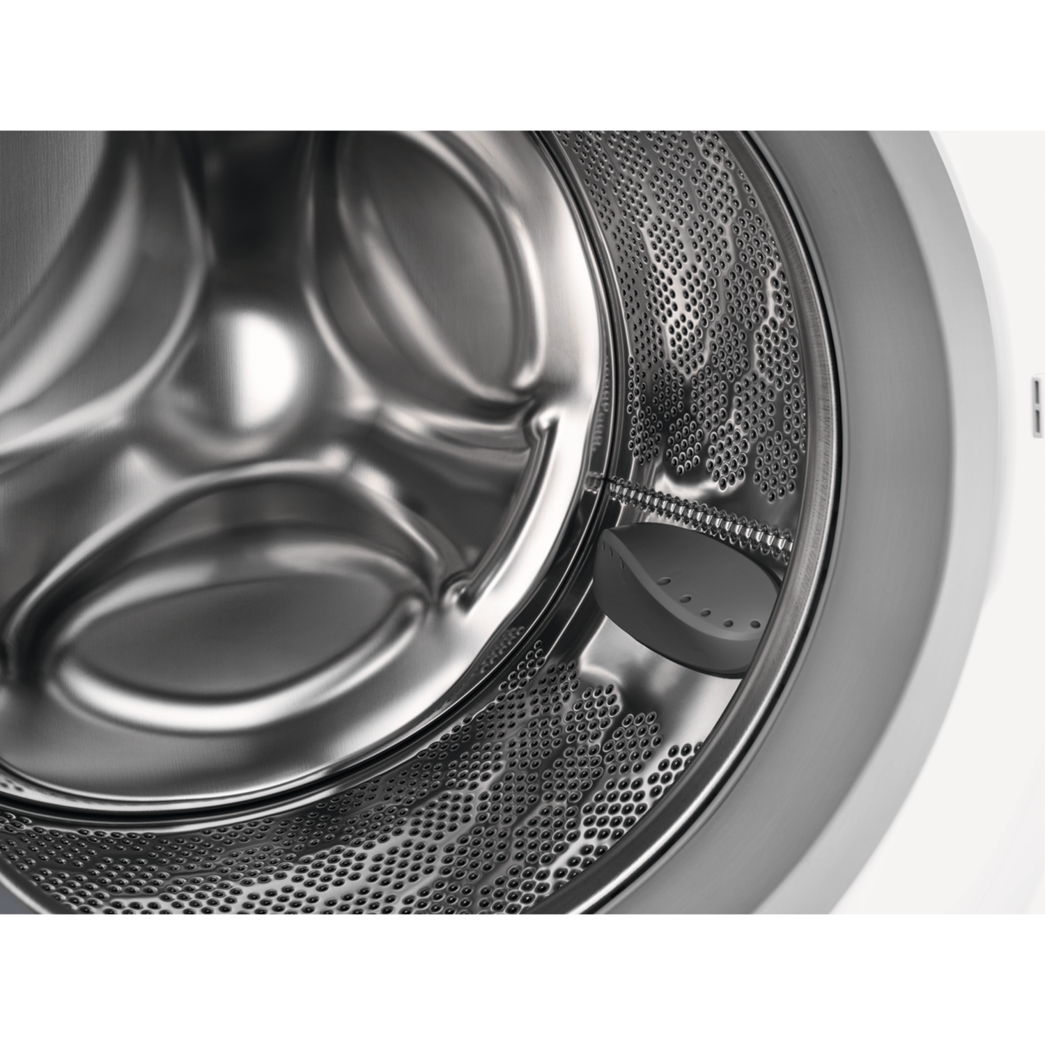 Close-up of the inside of a washing machine drum. It shows the perforated surface and a gray insert.
