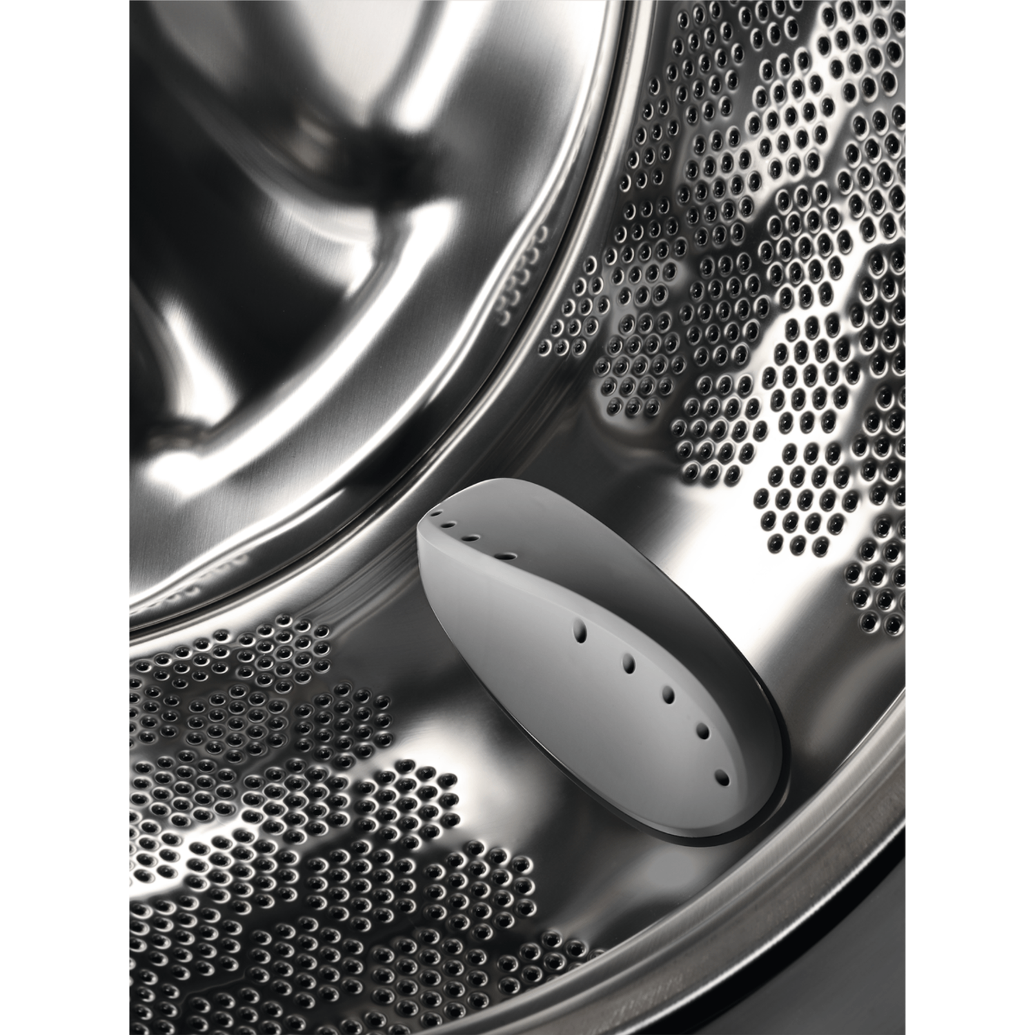 Close-up of the inside of a washing machine drum. It shows the perforated surface and a gray insert.