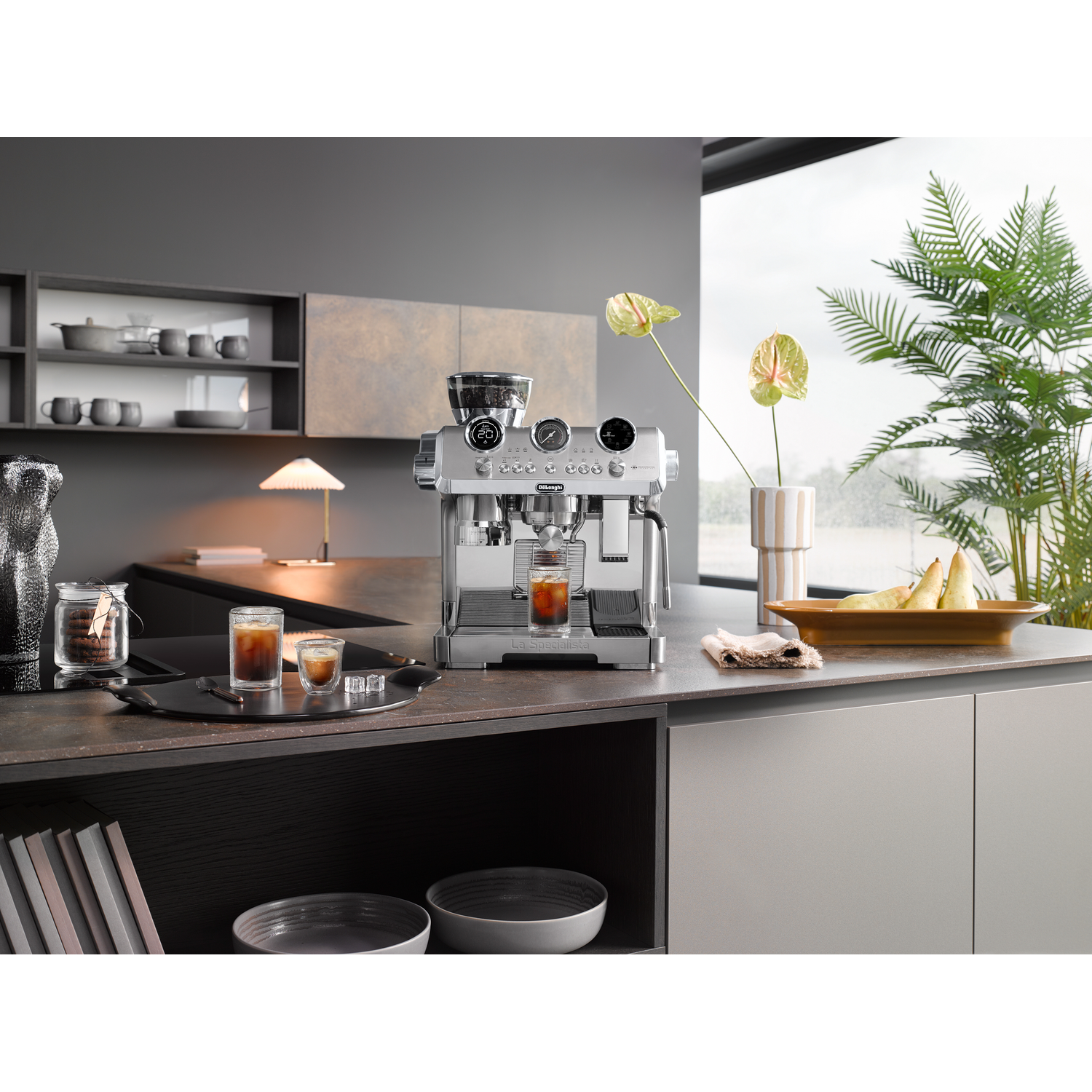 A coffee machine on a kitchen counter, next to glasses of coffee. A kitchen is in the background.