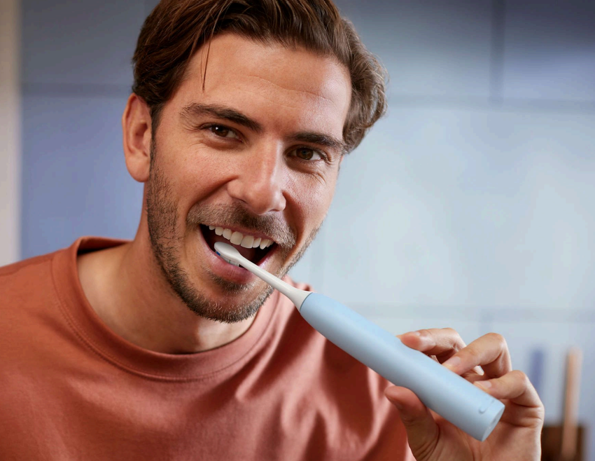 Egy barna inget viselő férfi világoskék Philips Sonicare fogkefével mos fogat.