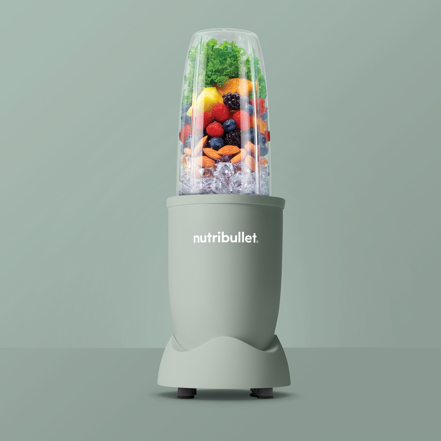 A green Nutribullet blender with fruits and ice cubes. On a green background.