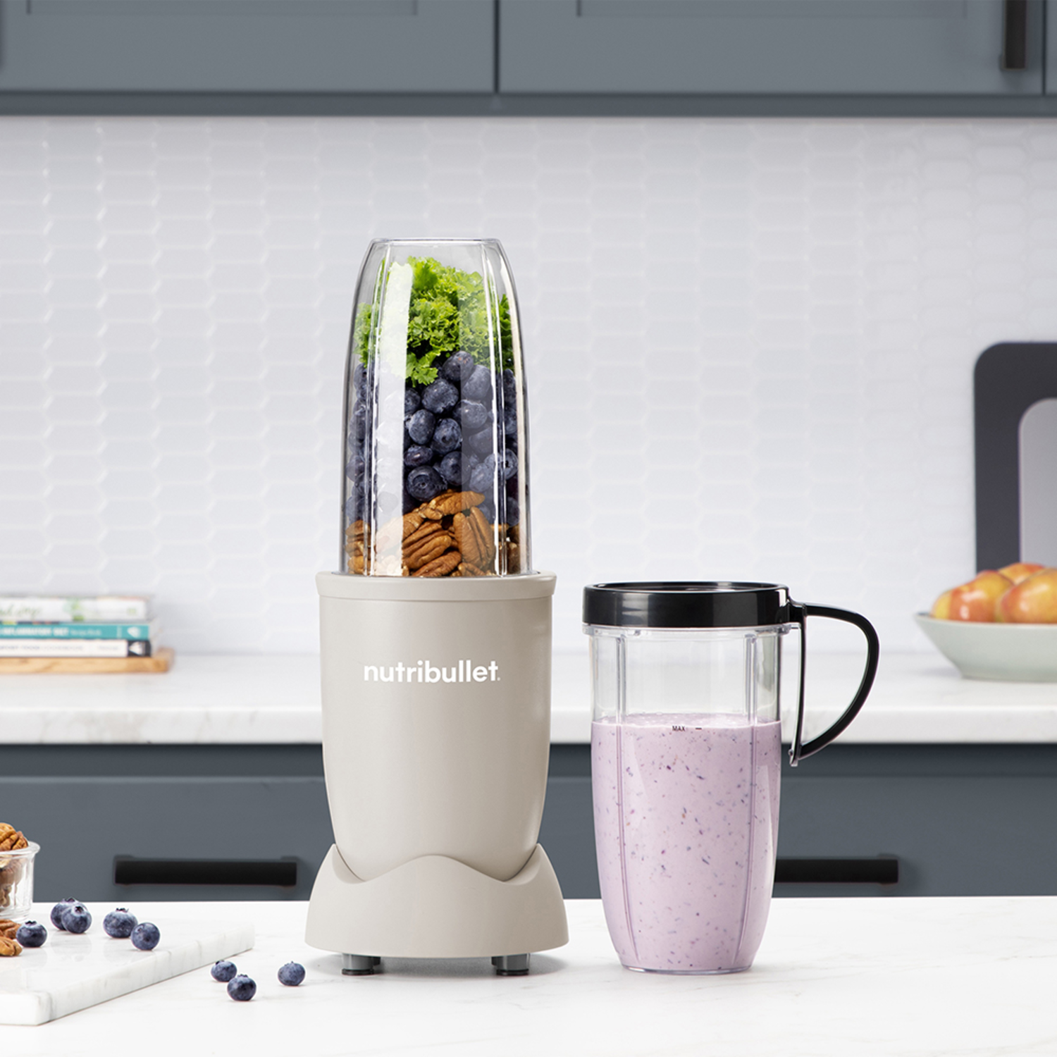Blender with blueberries, kale, and nuts. A smoothie cup with purple content next to it.