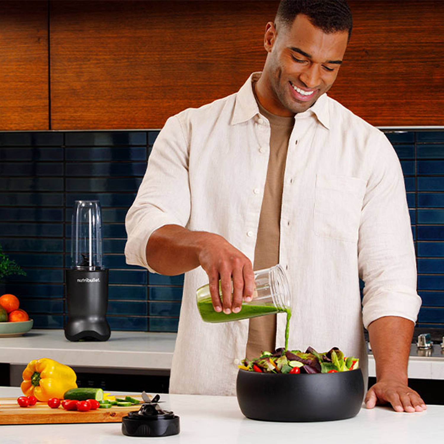 A man pouring green smoothie into a bowl of salad. Ingredients on the table.