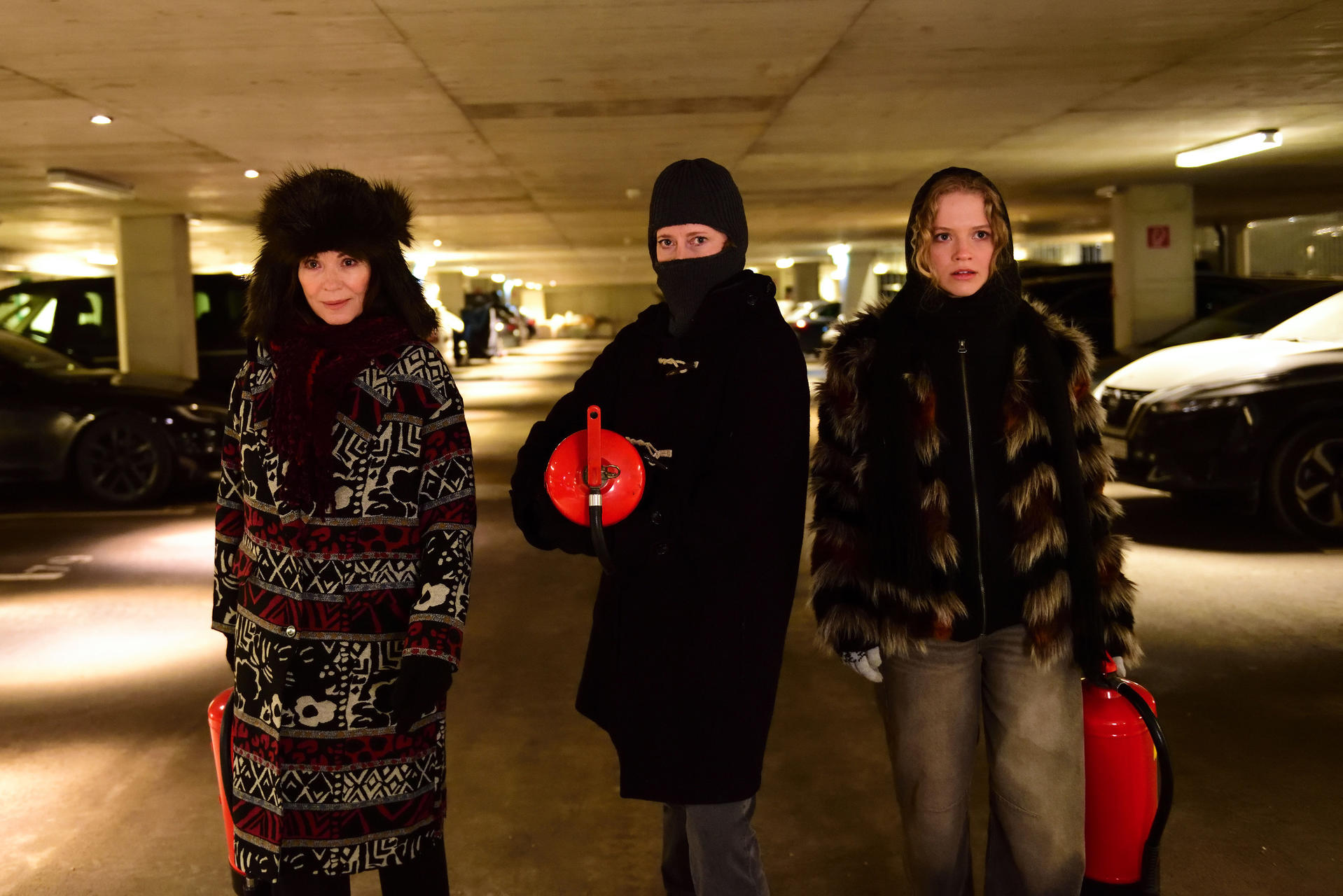 Drei Frauen stehen in einer Tiefgarage, zwei tragen Feuerlöscher.
