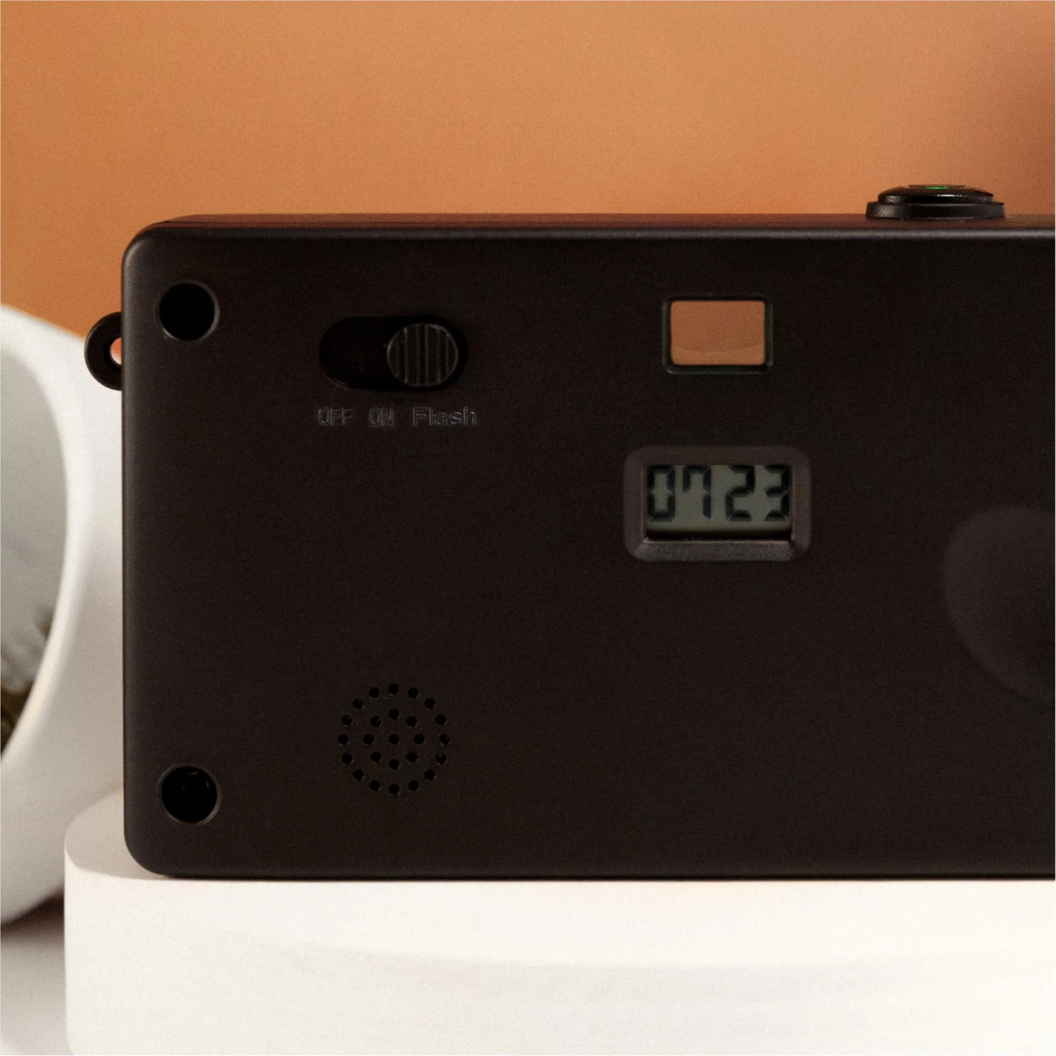 Black camera with an on/off/flash switch, digital display showing '0723', and a speaker. Set on a white surface.