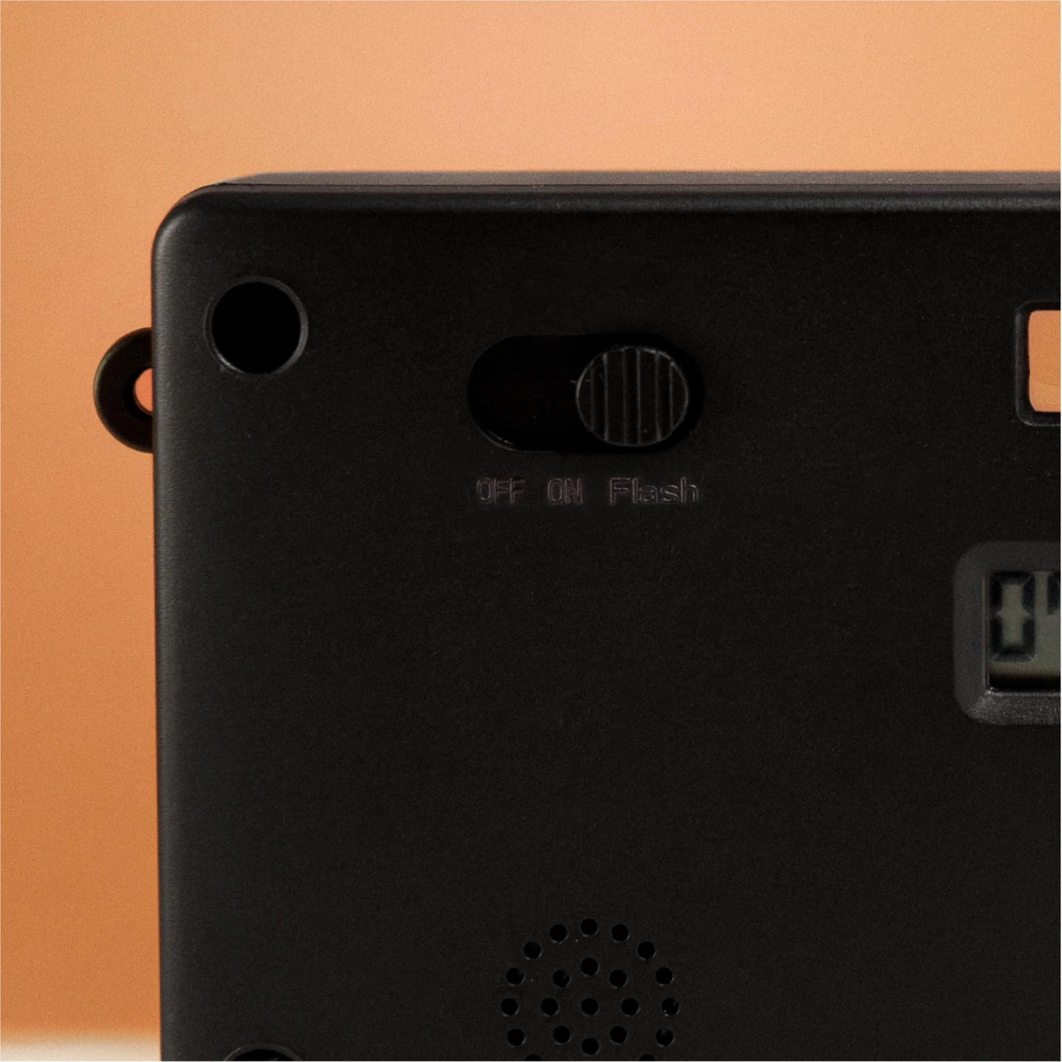 A close-up of a black device with a slider switch labeled 'OFF ON Flash'. There is a small digital display and a speaker.
