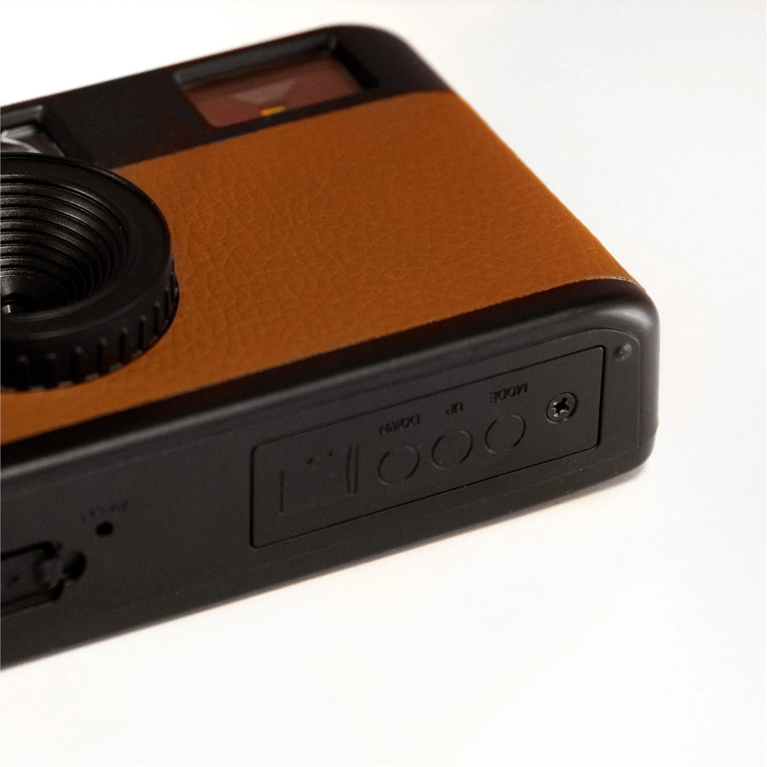 A black and brown camera is on a white surface. The camera has a lens, a brown leather-like top, and buttons on the side.