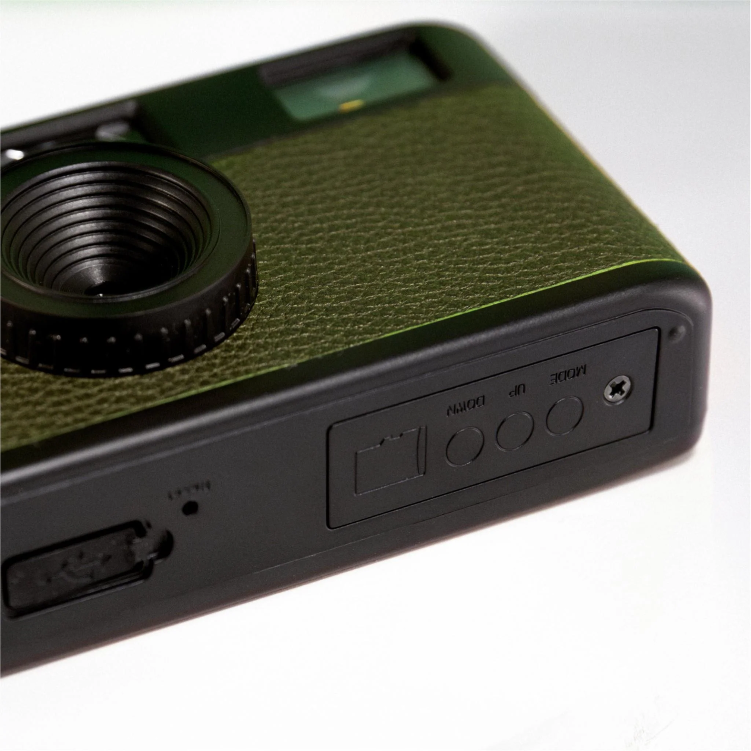 Close-up of a green and black camera. The lens is prominent, and the camera has a textured surface. Buttons and ports are visible.
