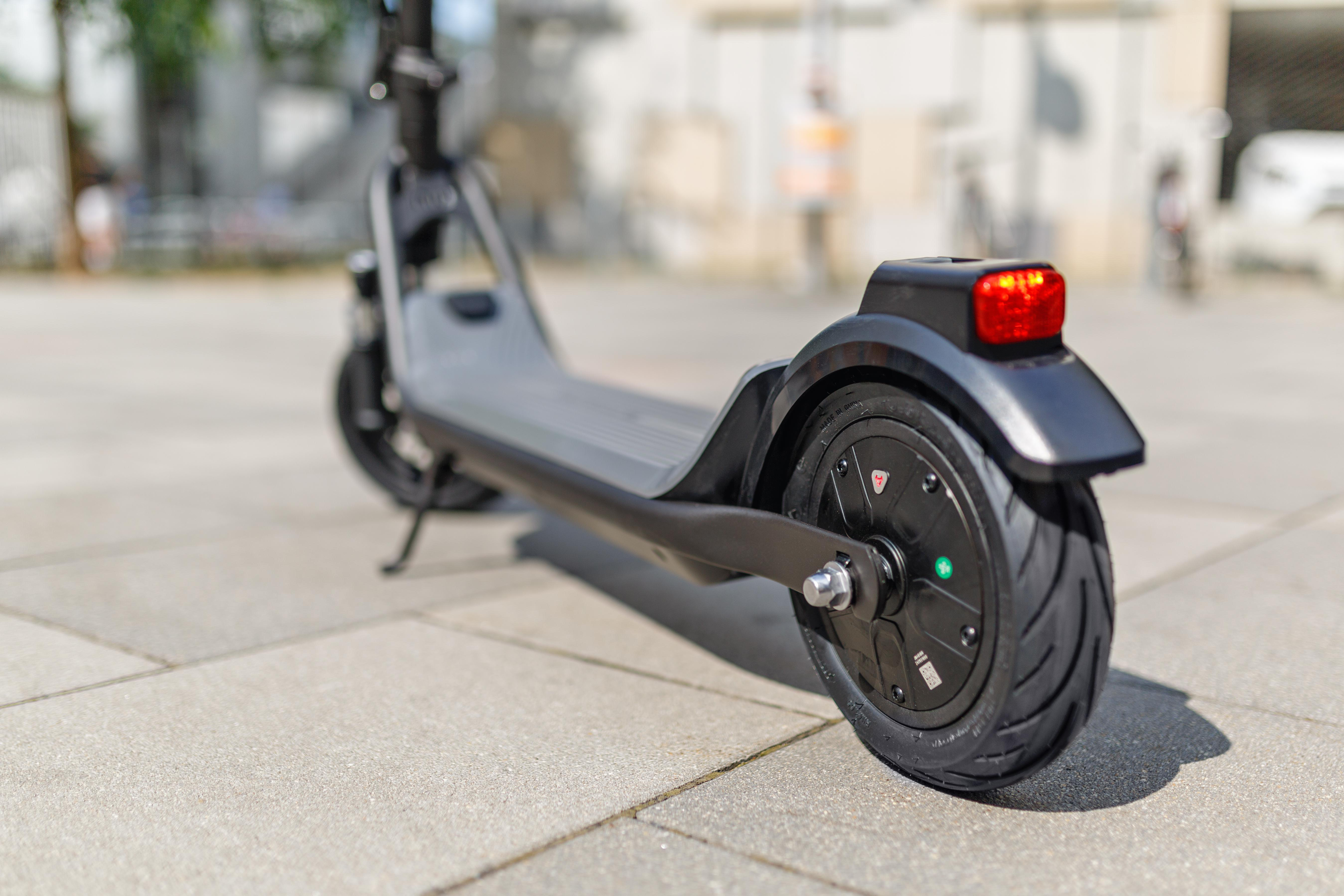 Rückansicht eines Elektrorollers auf einem Pflasterweg, mit rotem Rücklicht und Motor.