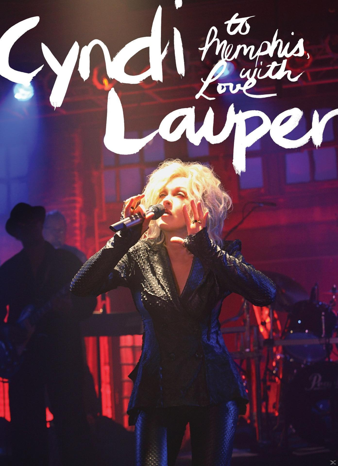 Cyndi Lauper singt auf einer Bühne, umgeben von Bühnenlicht und Musikern. Der Titel ist „Cyndi Lauper to Memphis with Love“.