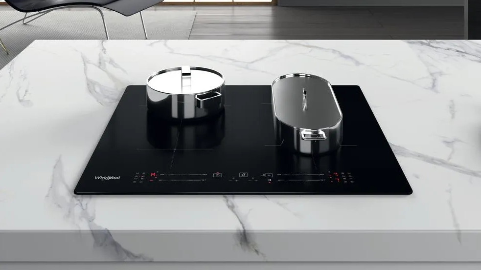 Czarna płyta indukcyjna z dwoma garnkami ze stali nierdzewnej na białym marmurowym blacie. Otoczenie kuchni.