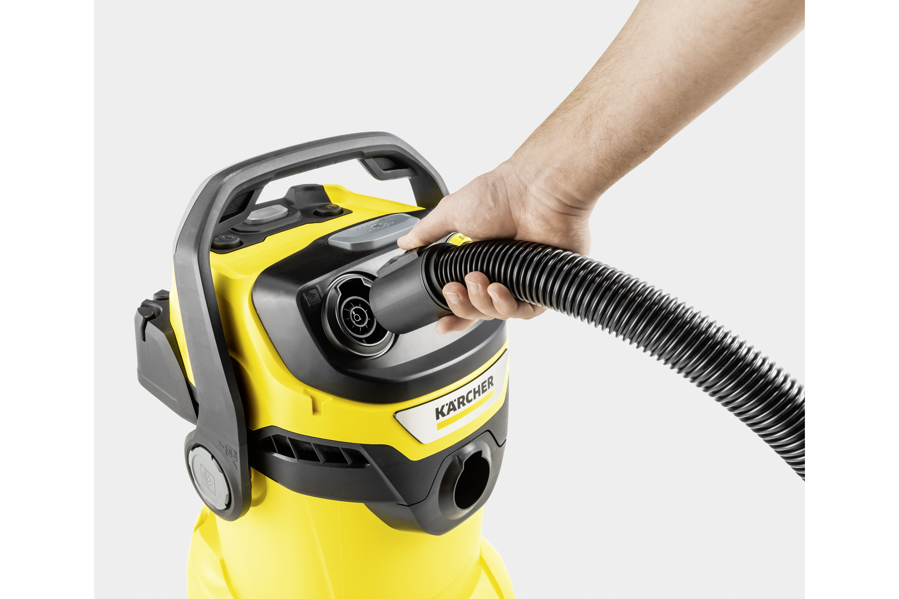 Ręka łączy wąż z żółtym odkurzaczem. Tło jest białe.