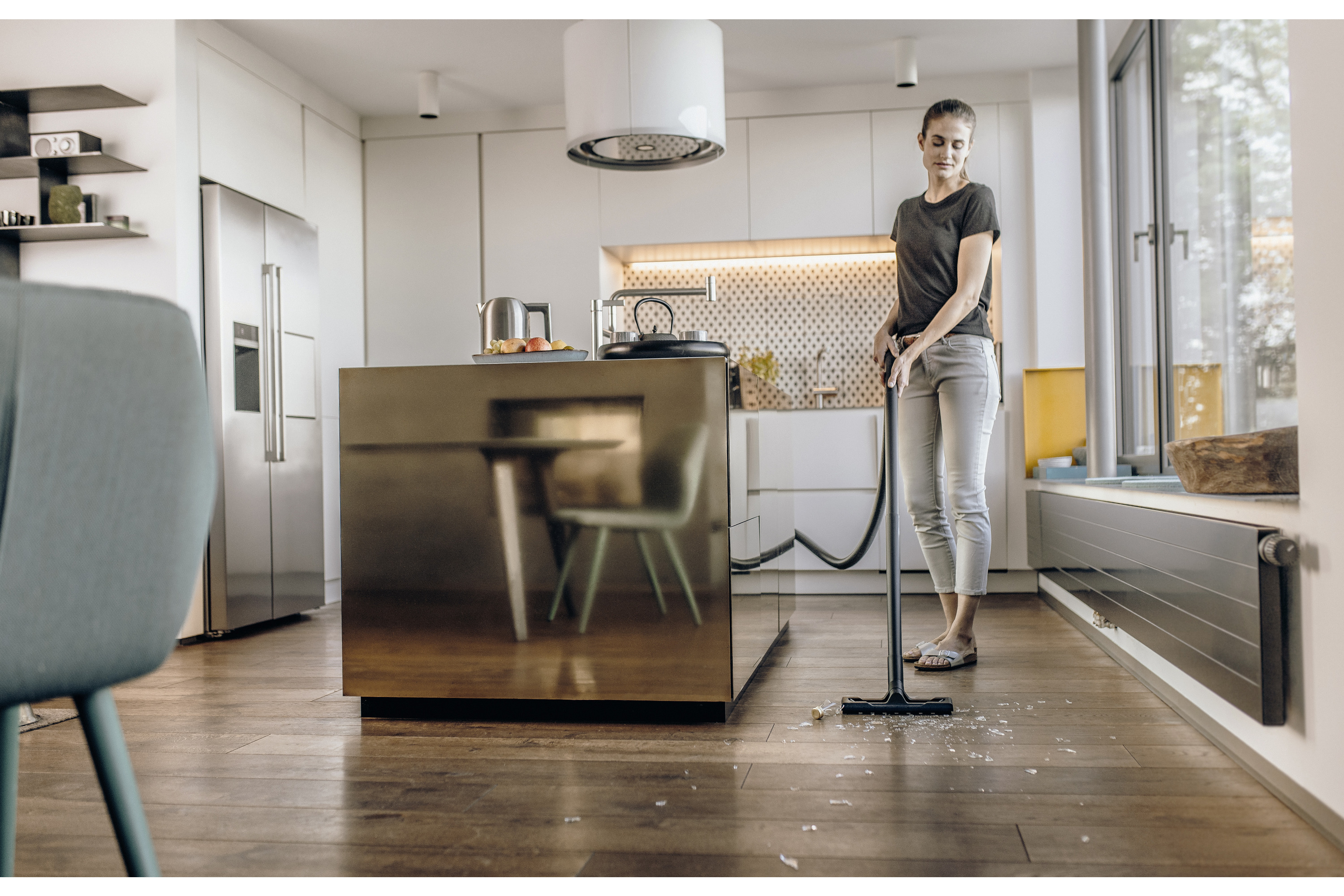 Kobieta odkurza w kuchni. Na podłodze leżą kawałki szkła.