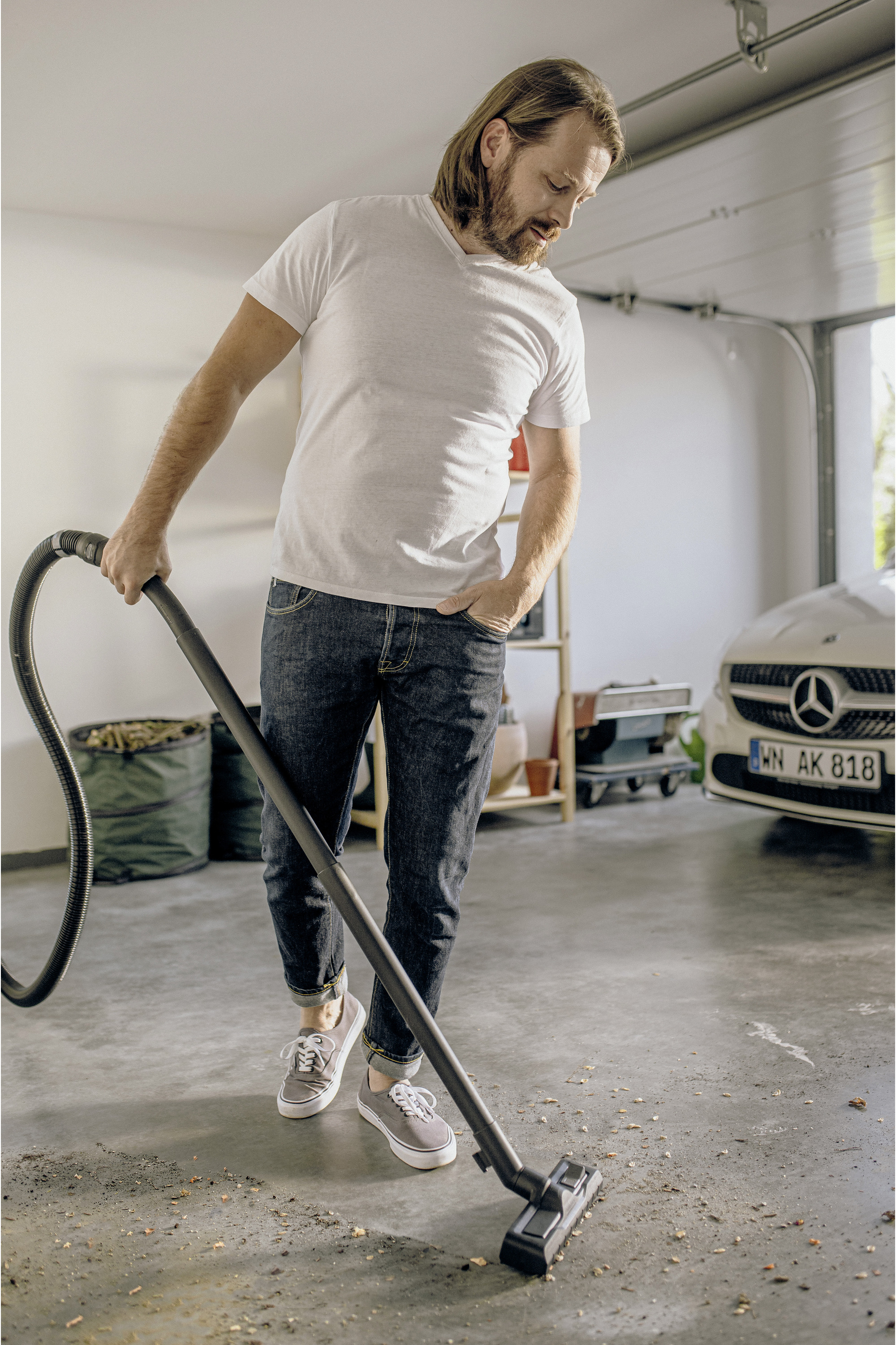 Mężczyzna odkurza garaż. Ma na sobie dżinsy i biały t-shirt.