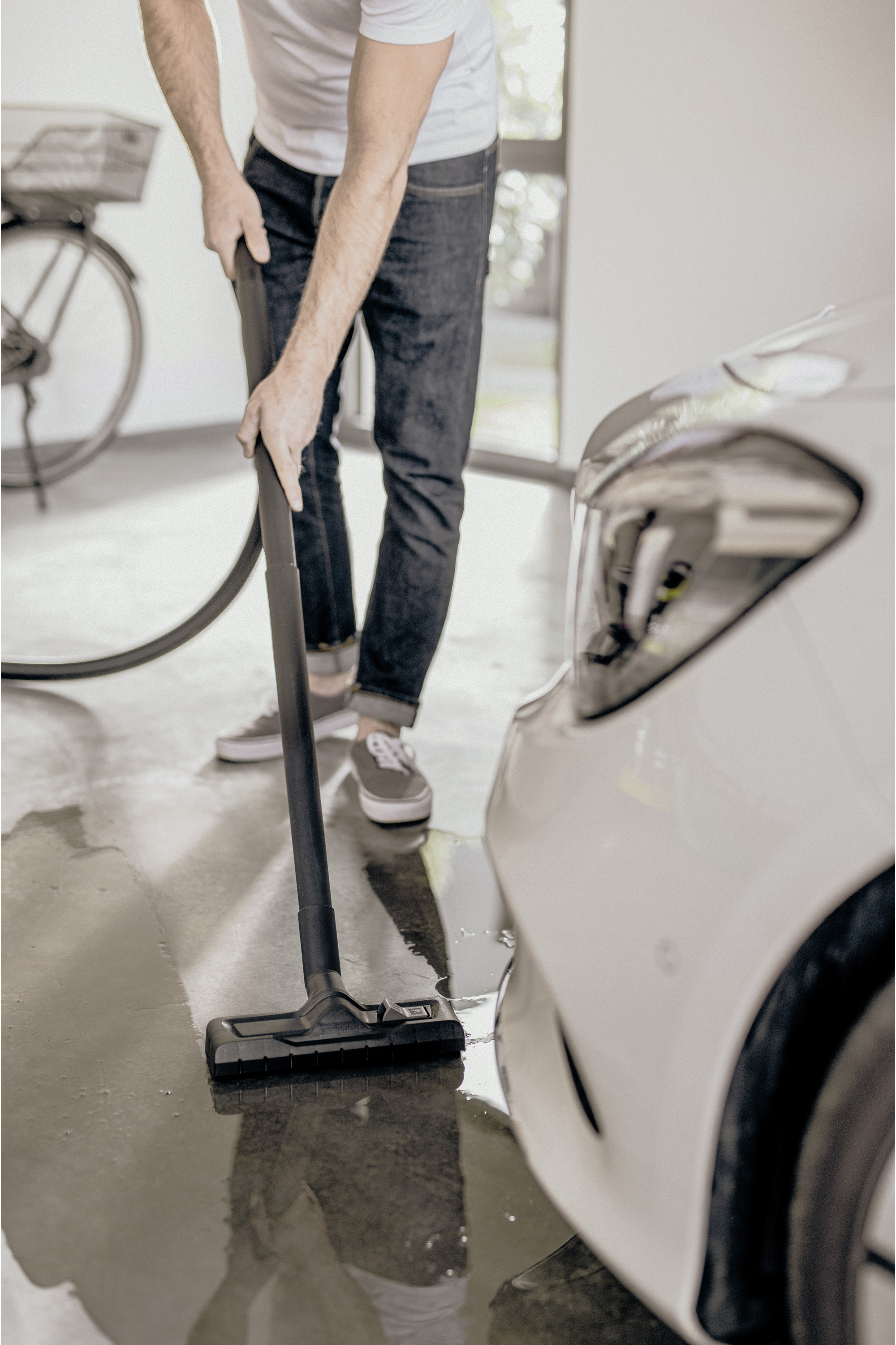 Mężczyzna odkurza podłogę w garażu. Obok stoi biały samochód. W tle widać rower.