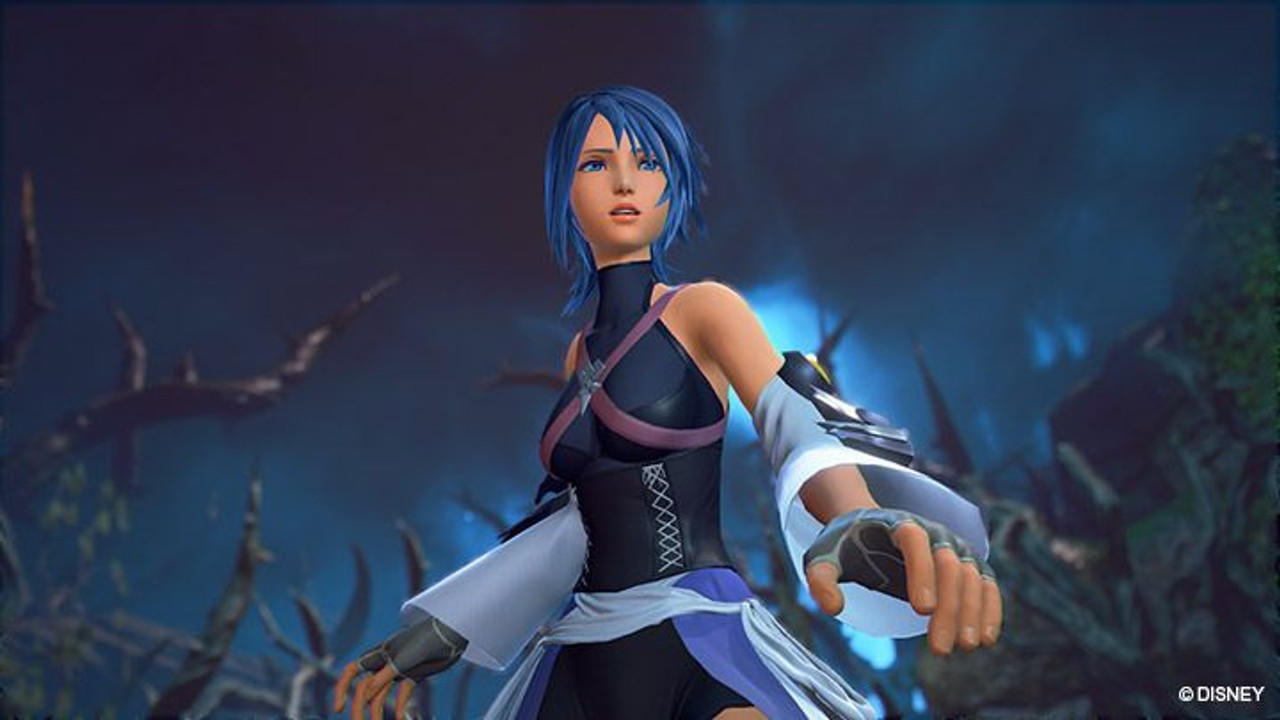 Aqua, eine blauhaarige Frau in Schwarz-Weiß, steht in einem dunklen Wald. Im Hintergrund sind dunkle Bäume und blauer Himmel zu sehen.