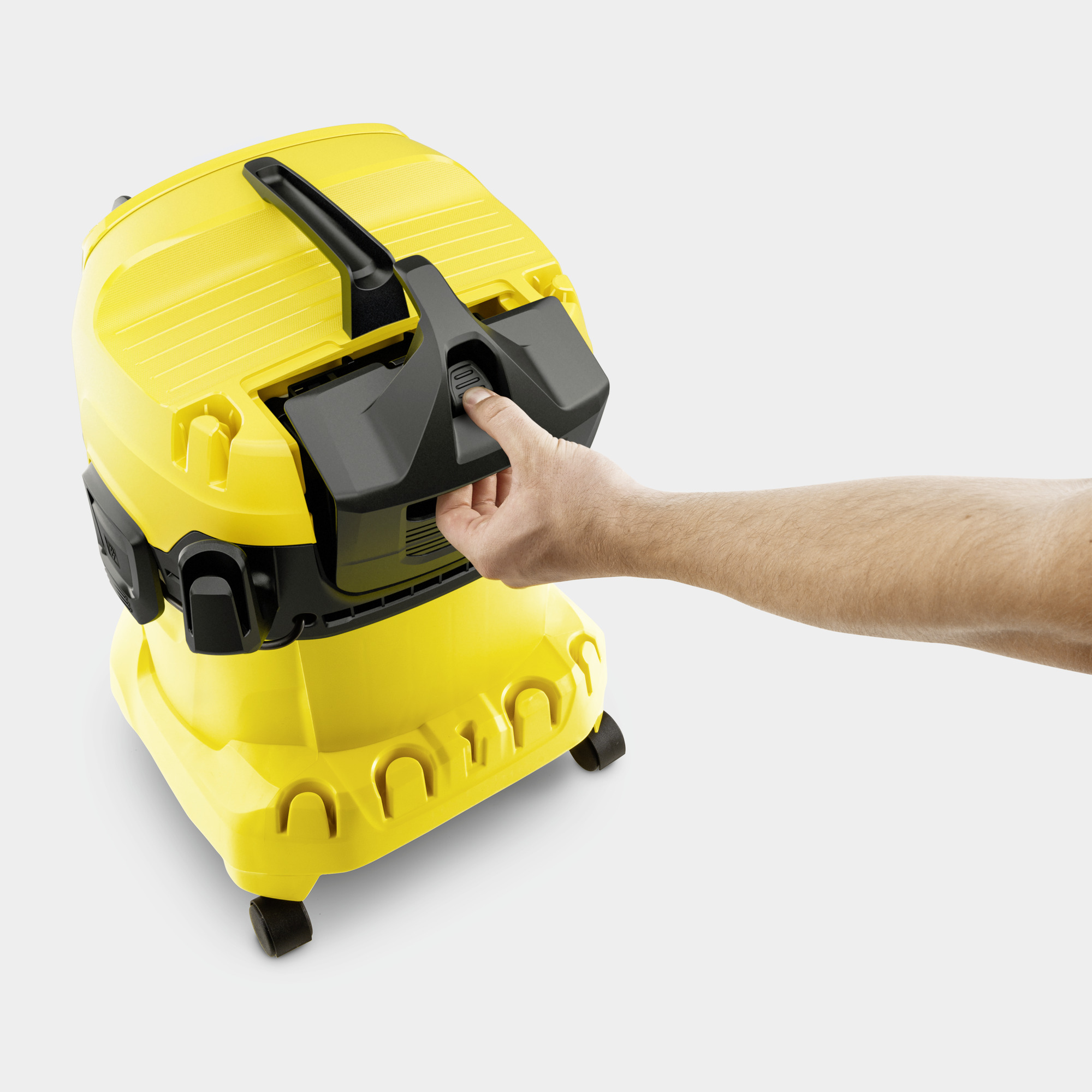 Osoba otwiera żółty odkurzacz Kärcher, czarna pokrywa, białe tło.