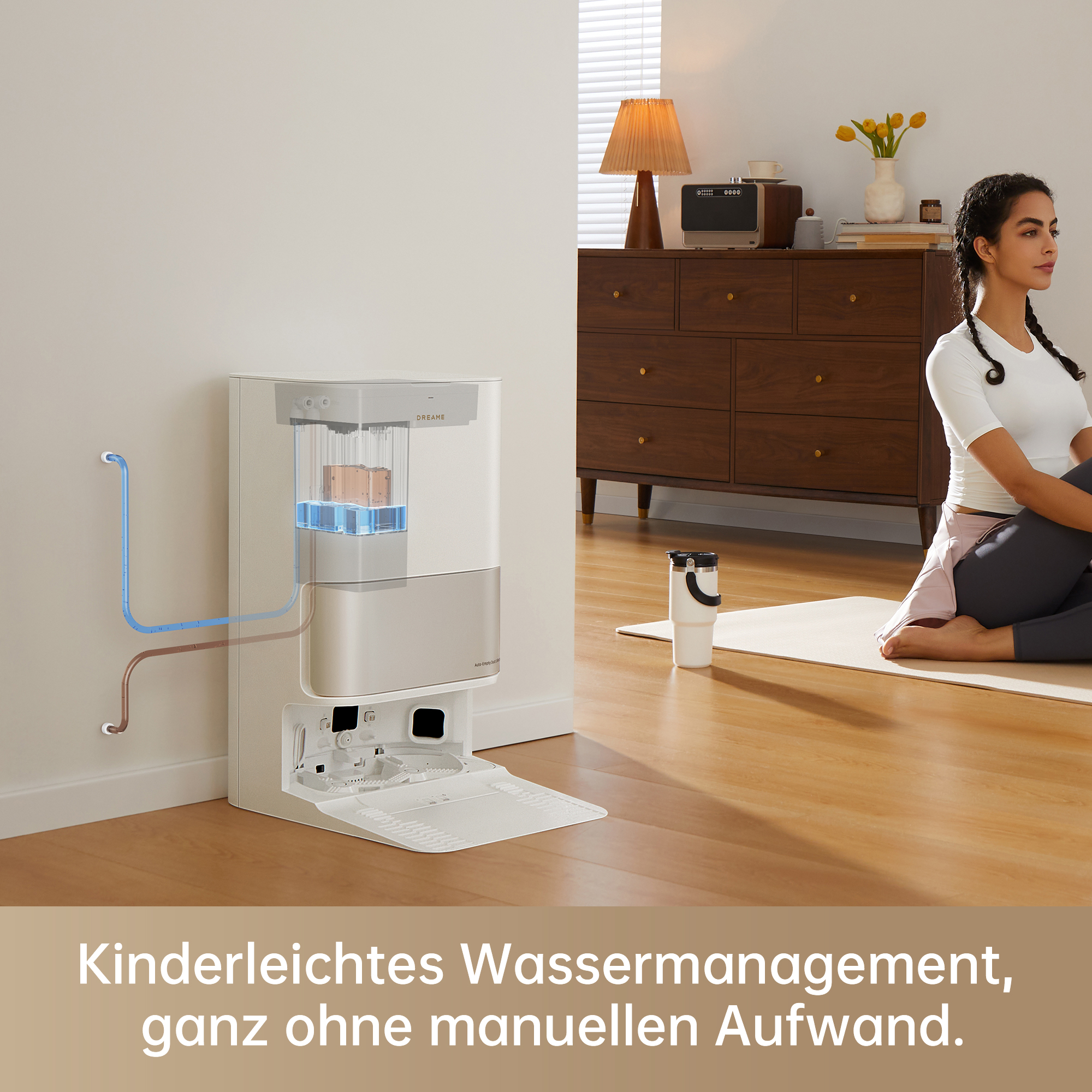 Eine Frau sitzt auf einer Matte, neben einem Roboter-Staubsauger und einem Wasser-Management-System, in einem Raum.