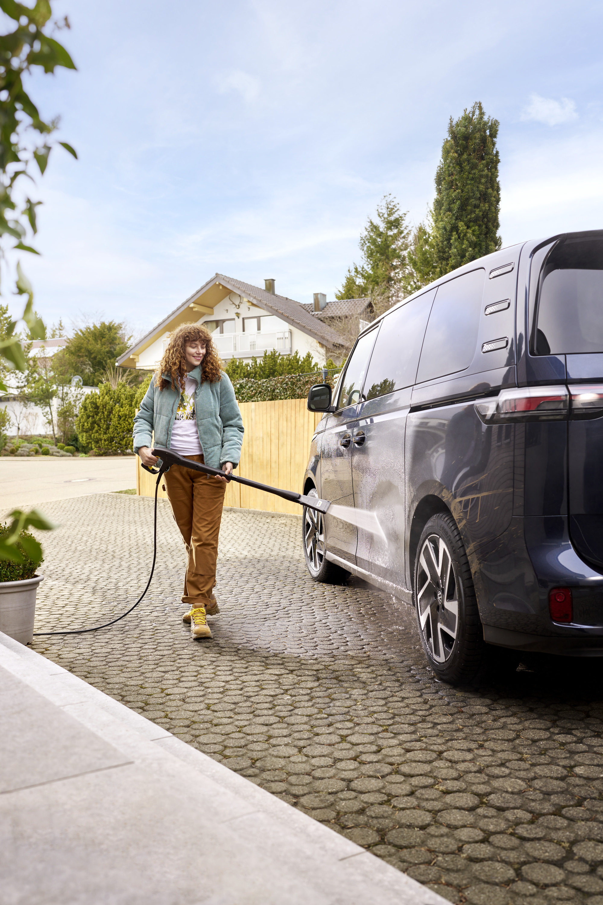 Kobieta myjąca samochód myjką ciśnieniową przed domem.